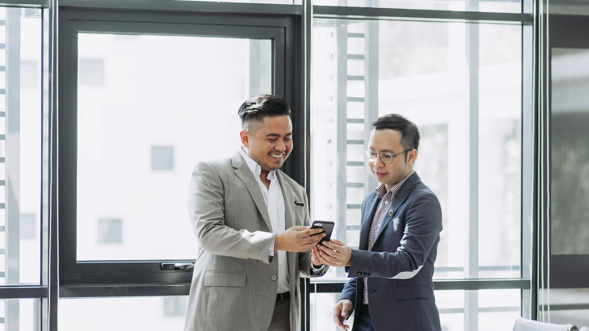 a couple of men in suits looking at a cell phone
