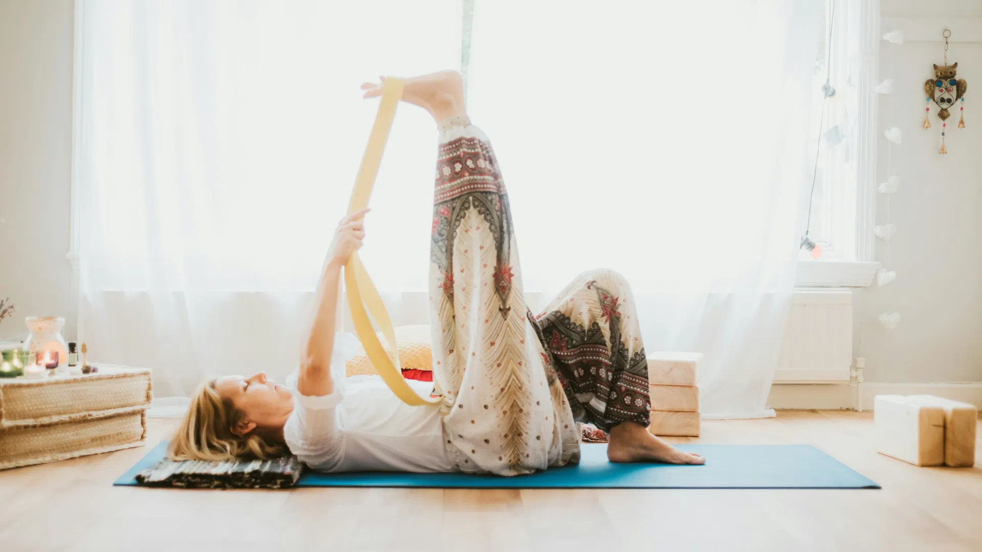 Woman practicing yoga indoors on a mat using a strap to stretch her leg in a bright, peaceful room.