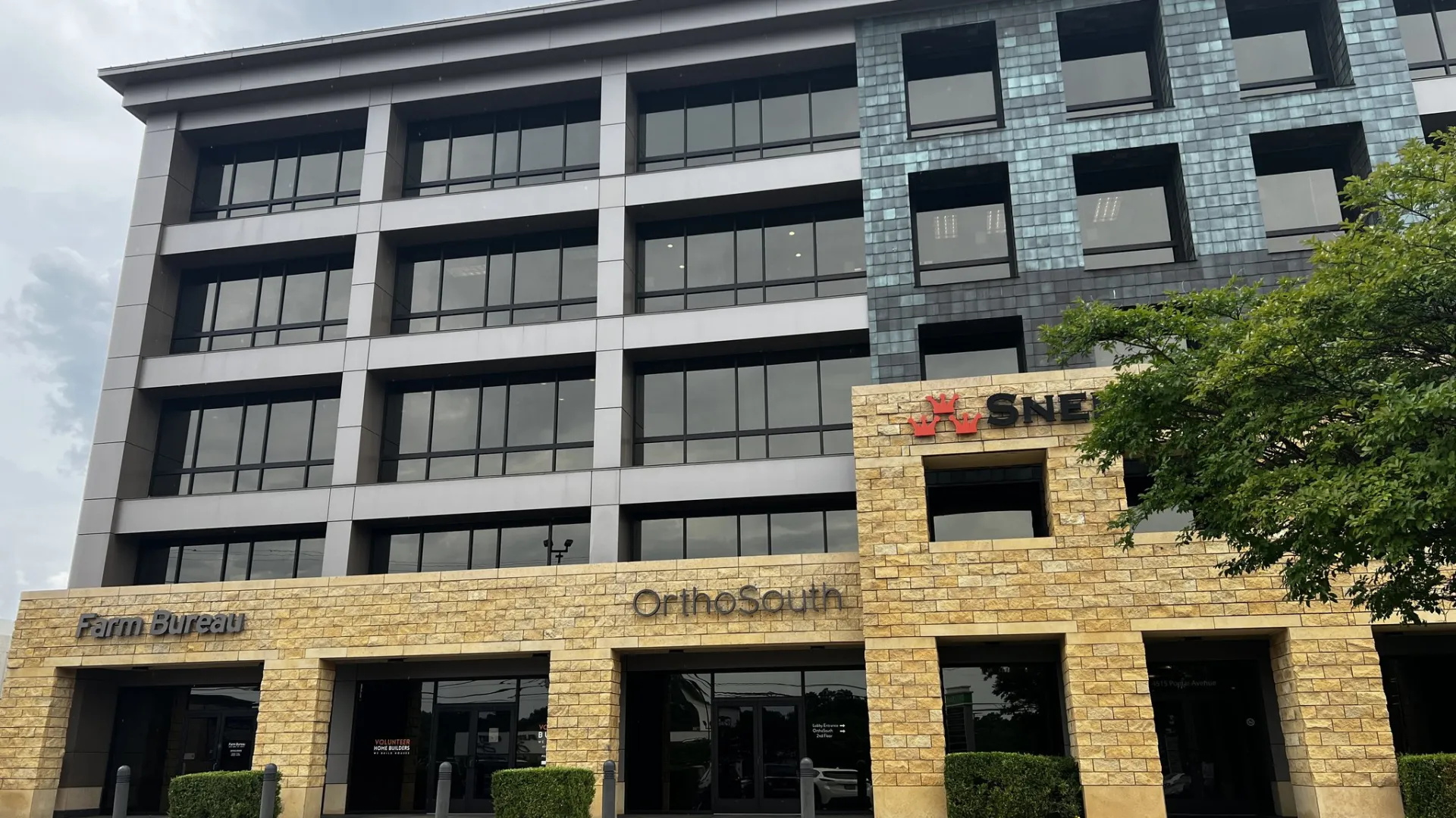 Front view of a multi-story office building with stone and glass facade under a cloudy sky.