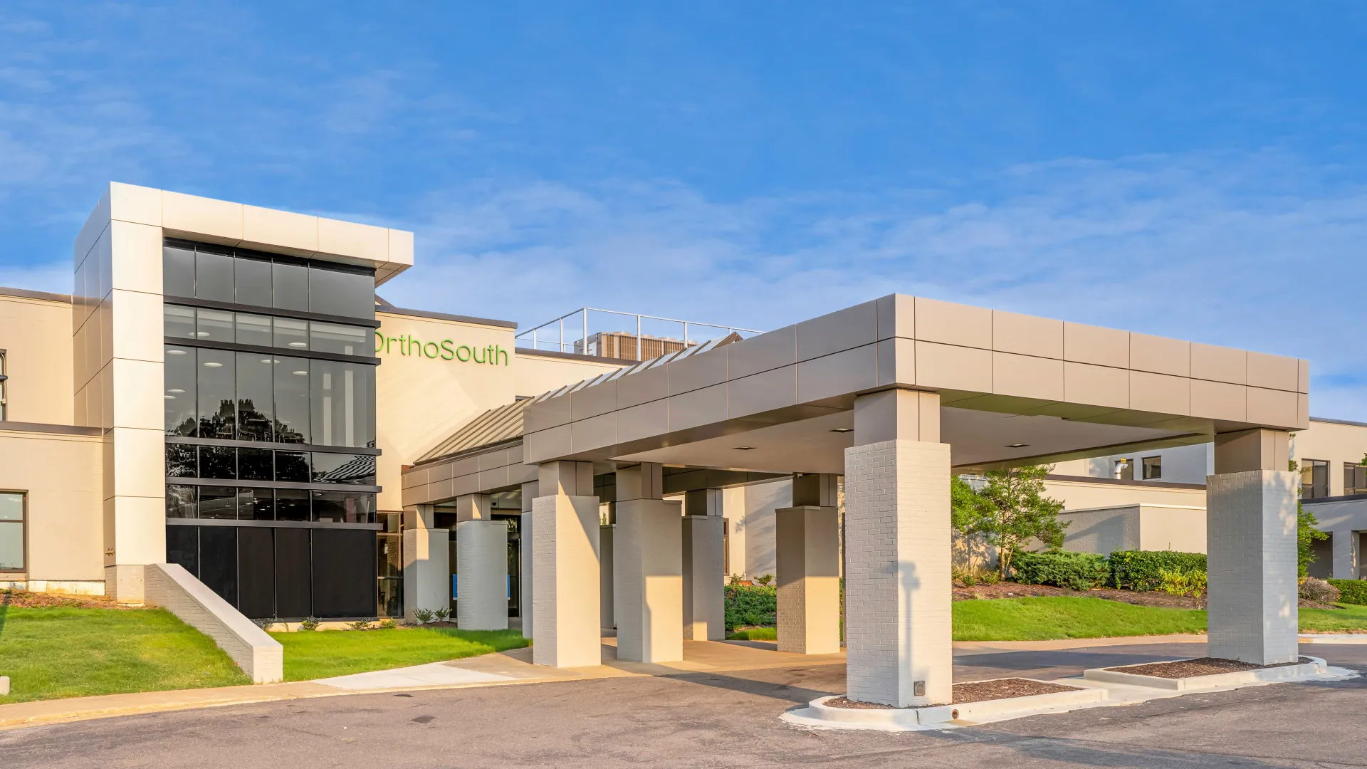 Modern medical building with large glass windows and covered entrance under clear blue sky.