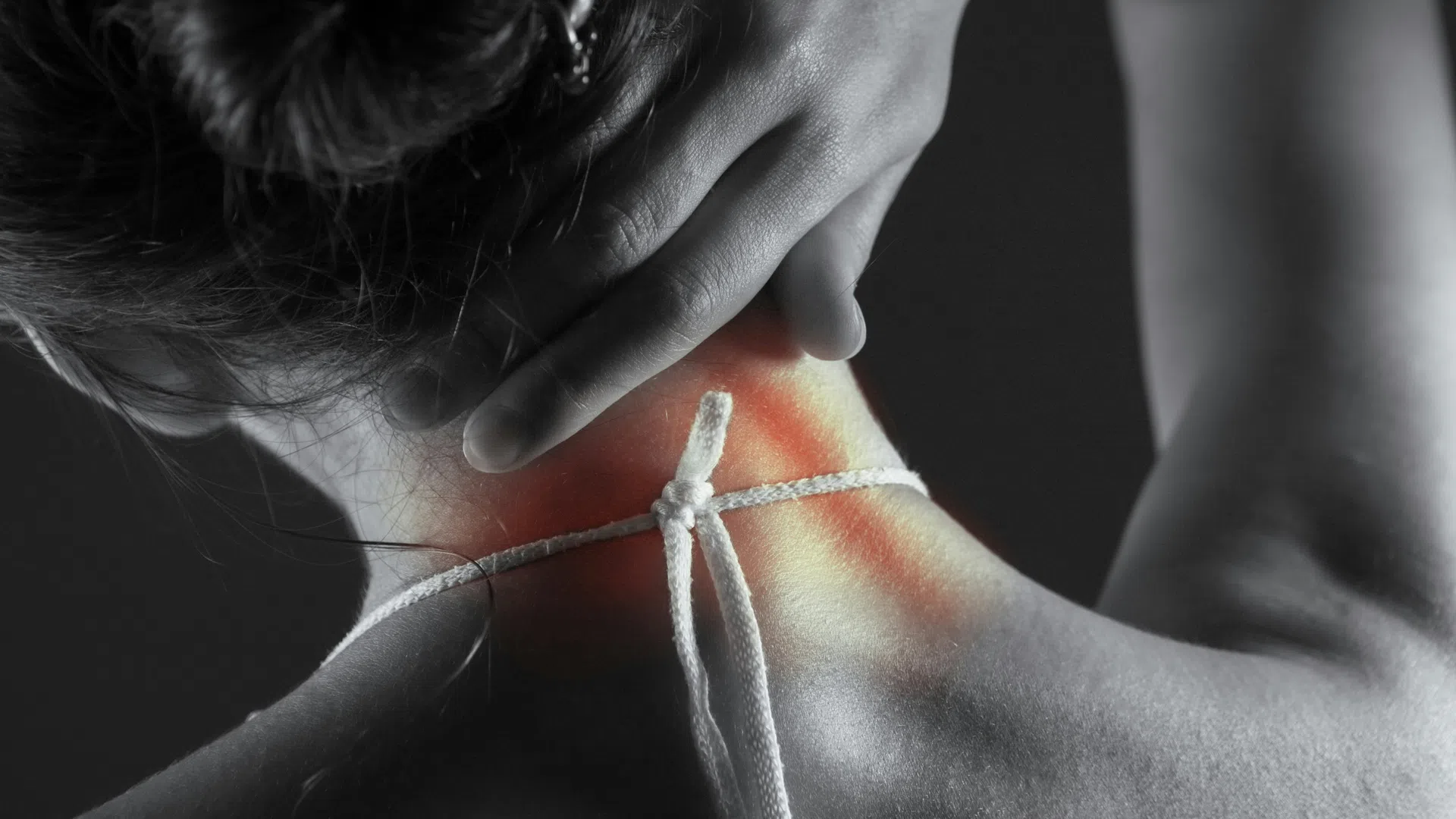 Person holding neck with highlighted red area indicating neck pain or discomfort in black and white photo.