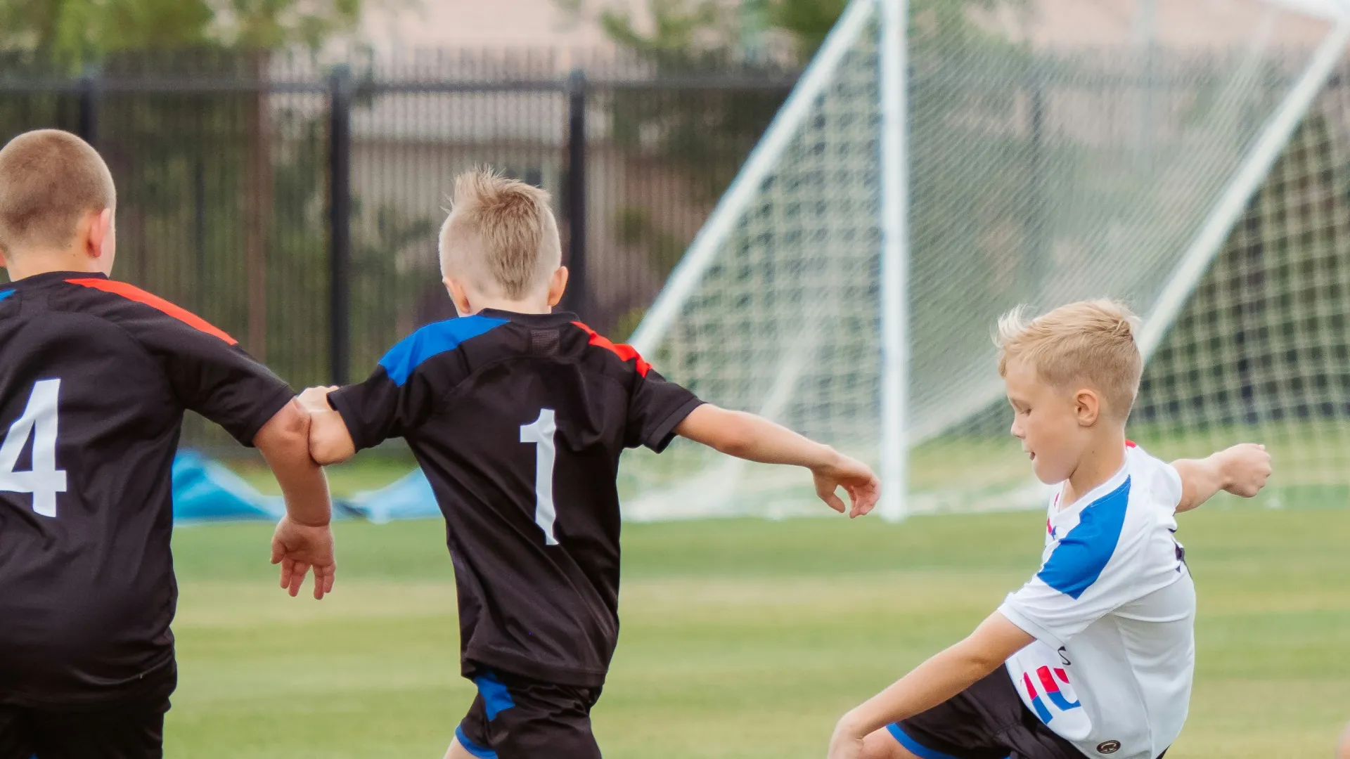 Young boys playing soccer, dribbling a ball on a grassy field with goalposts in the background.