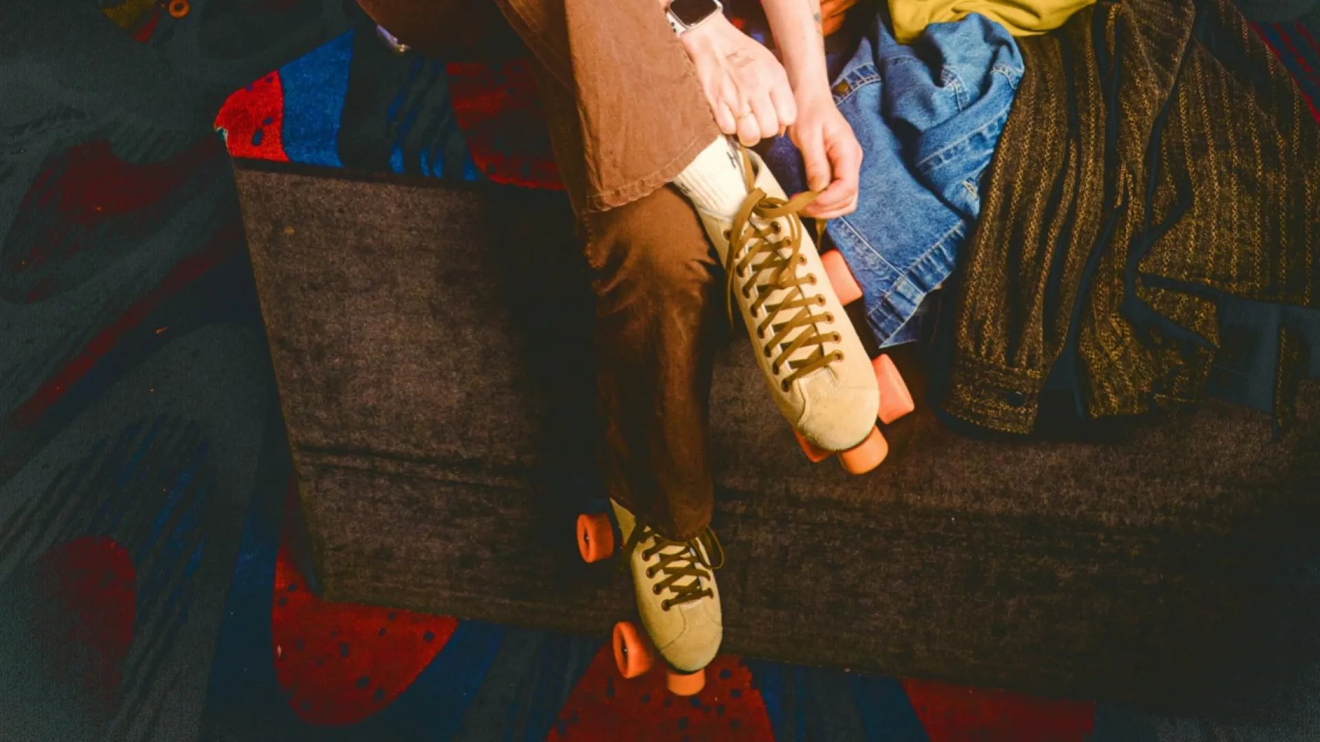 Smiling young woman putting on roller skates at indoor roller rink with colorful lighting and other skaters in background