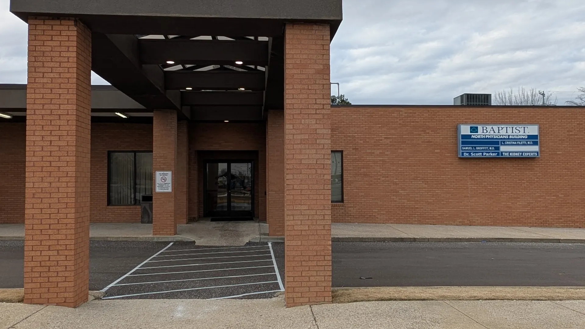Entrance of a brick Baptist North Physician building with a covered walkway and designated parking spots.