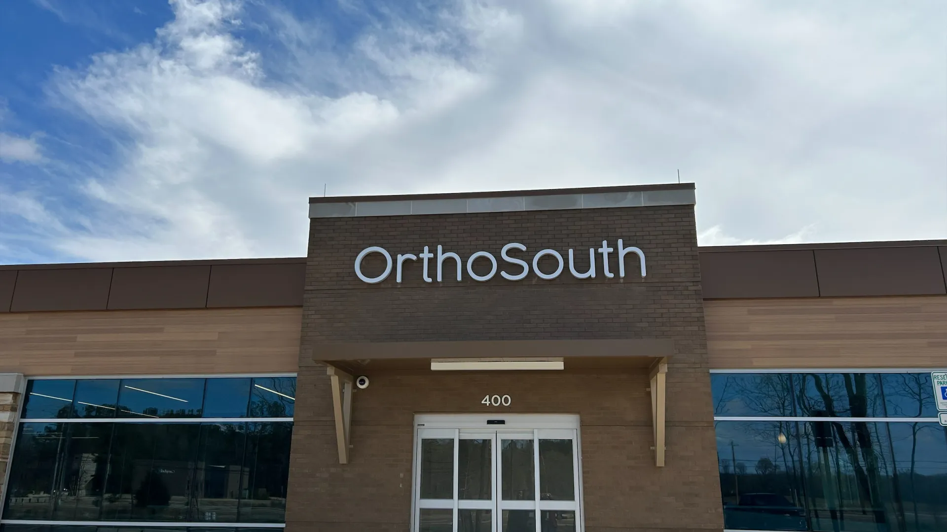 Front entrance of OrthoSouth clinic building under partly cloudy sky