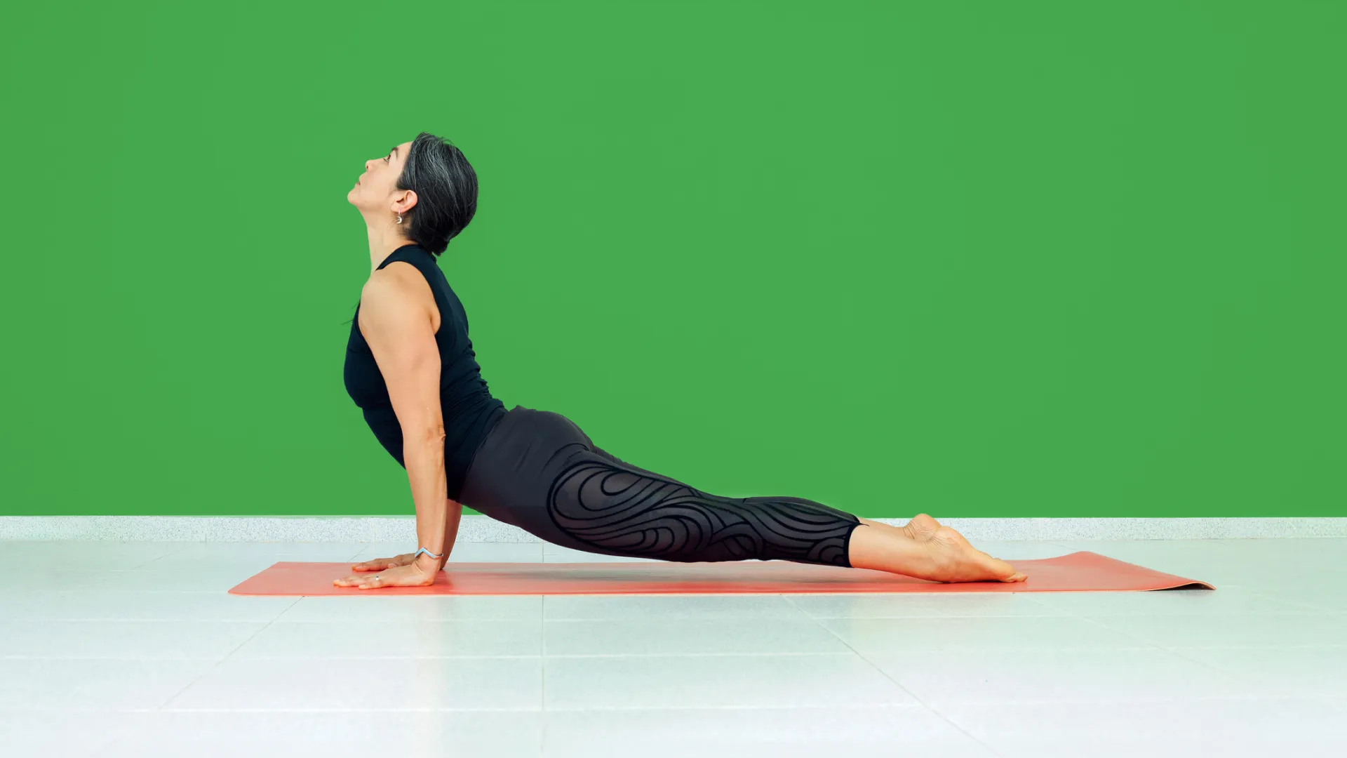 A woman in a yoga pose on an orange mat, set against a vibrant green wall, showcasing elegance and strength.