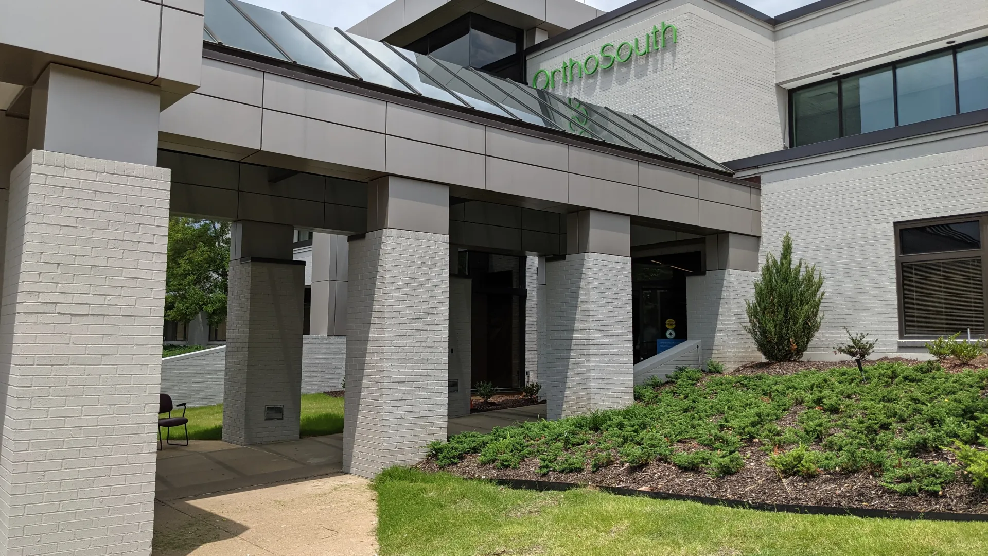 Modern orthopedic clinic entrance with green signage and landscaped surroundings.