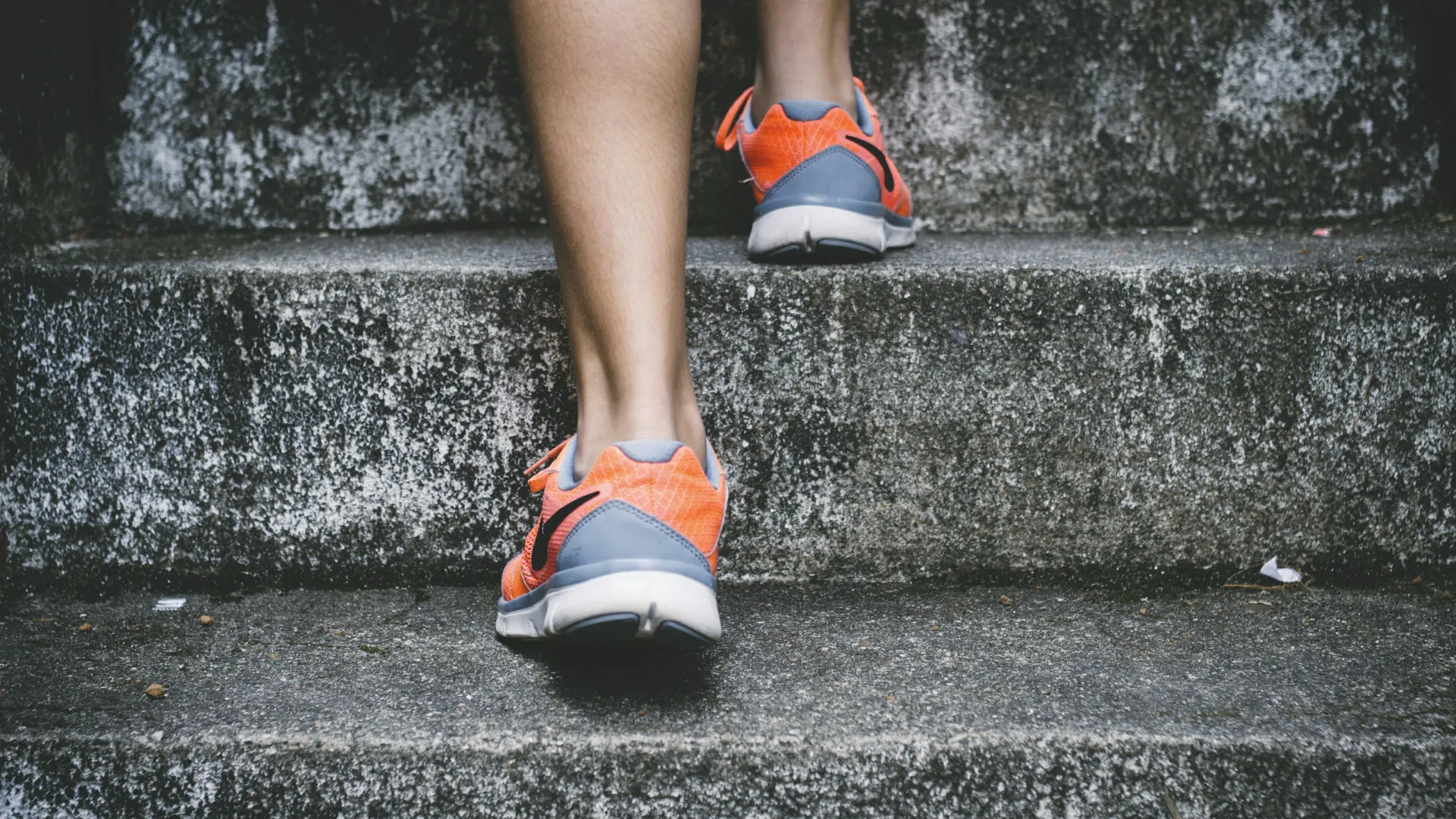 Person wearing orange athletic shoes walking up concrete stairs during exercise or training.