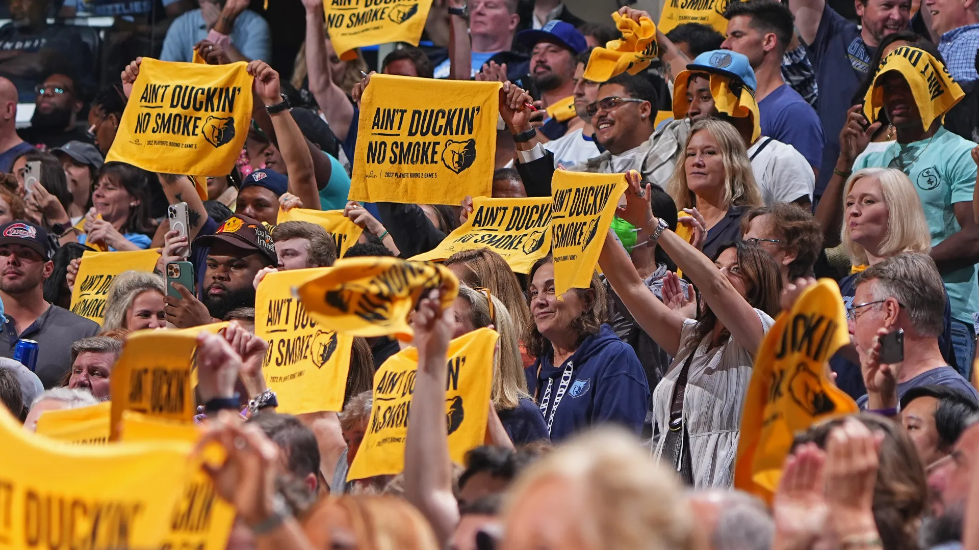 Energetic crowd at a Memphis Grizzlies game holding yellow rally towels with 'Ain't Duckin No Smoke' slogan.
