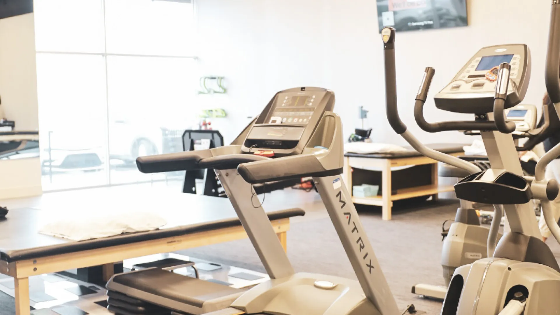 Modern gym interior featuring treadmill and elliptical machine with natural light and sleek design.