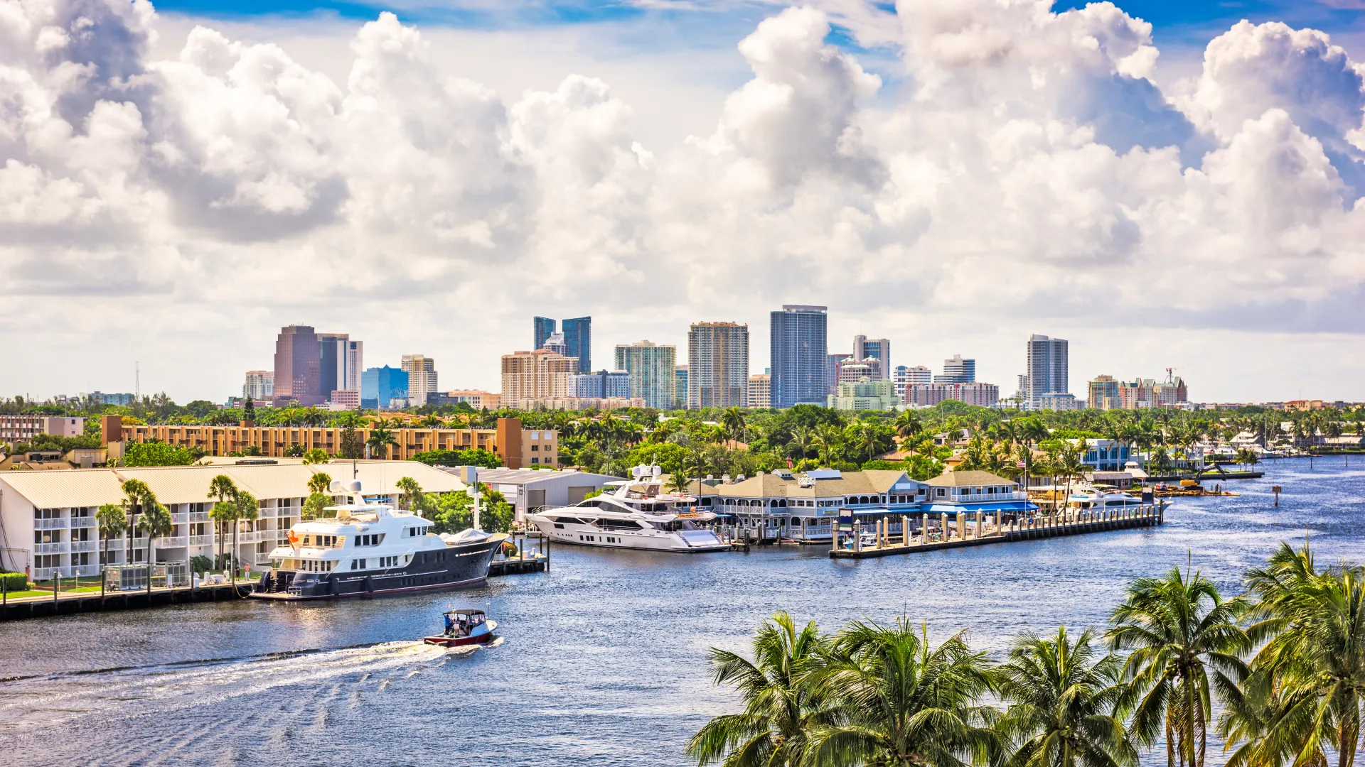 Scenic view of Fort Lauderdale's skyline along the water with boats and palm trees under a vibrant sky.