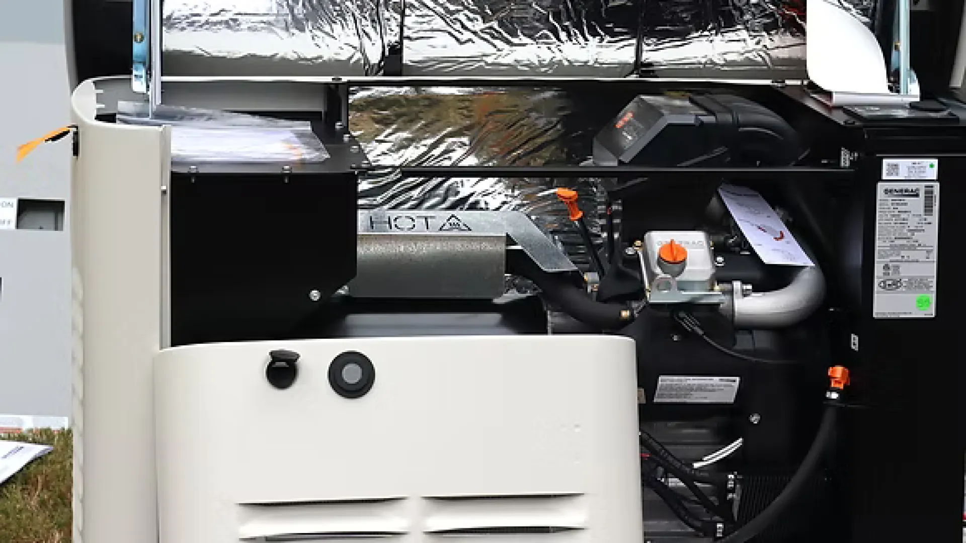 Open industrial generator showing internal components including pipes, engine, and insulation panels.