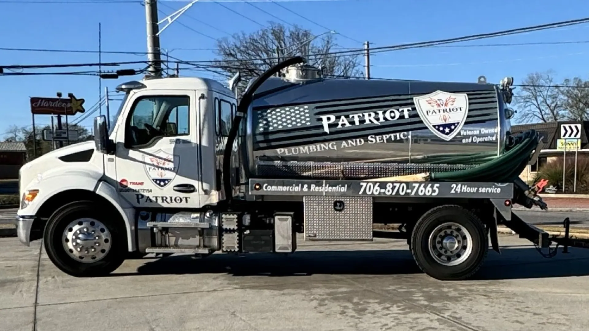 White Patriot Plumbing and Septic service truck with trailer carrying equipment parked on concrete under clear blue sky.