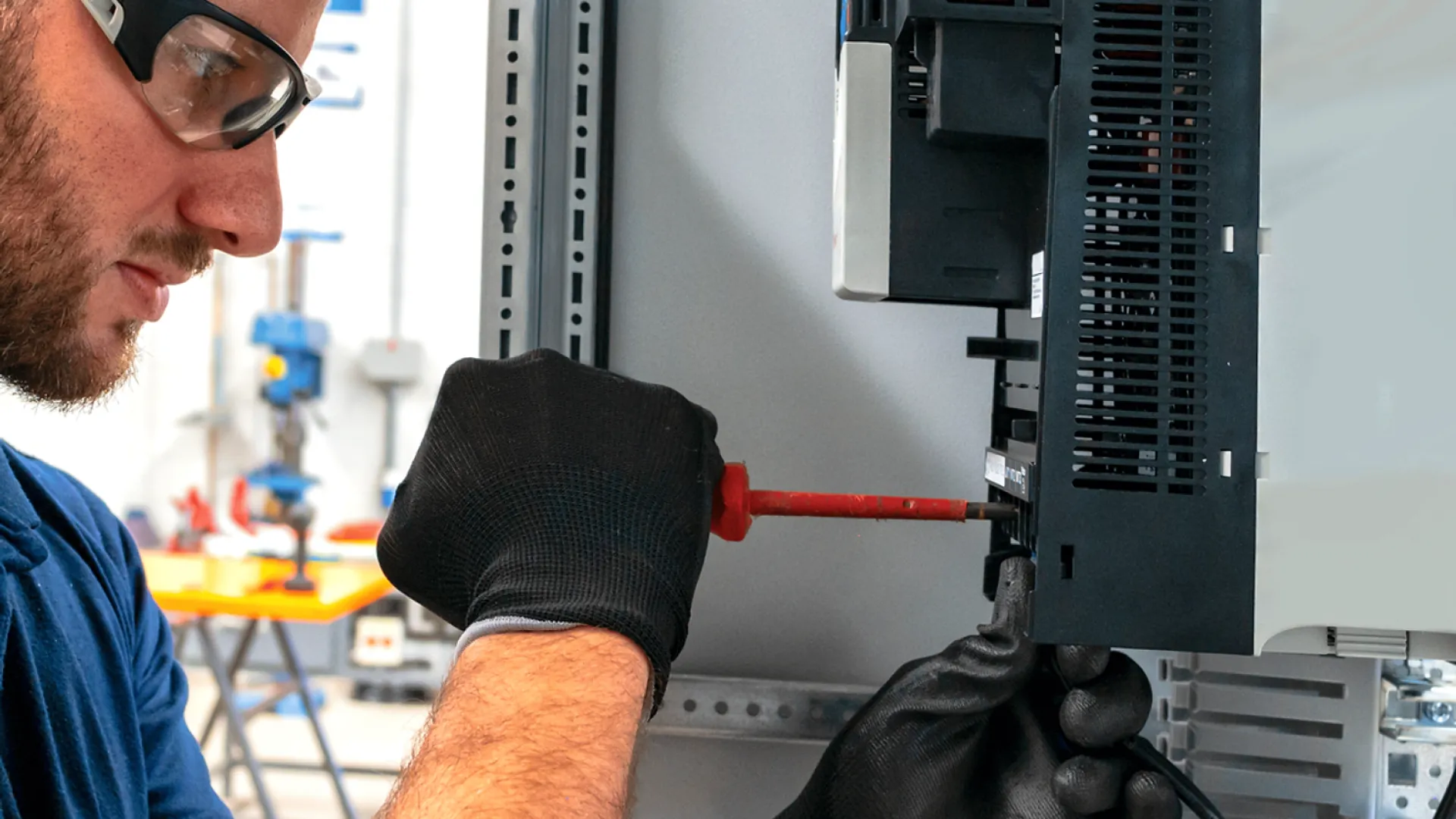 Technician wearing gloves and safety glasses working on electrical control panel with screwdriver