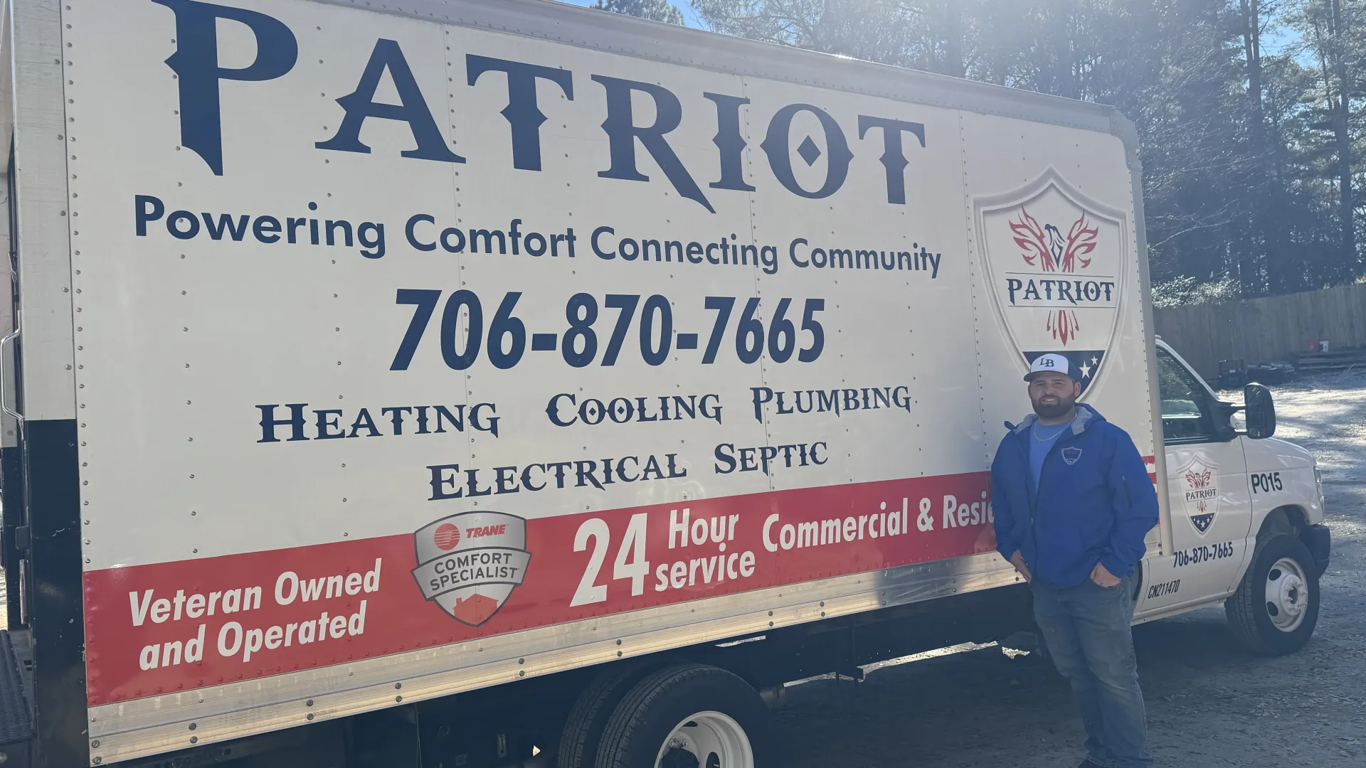 Man standing next to Patriot service truck advertising heating, cooling, plumbing, electrical, septic services and 24-hour support.
