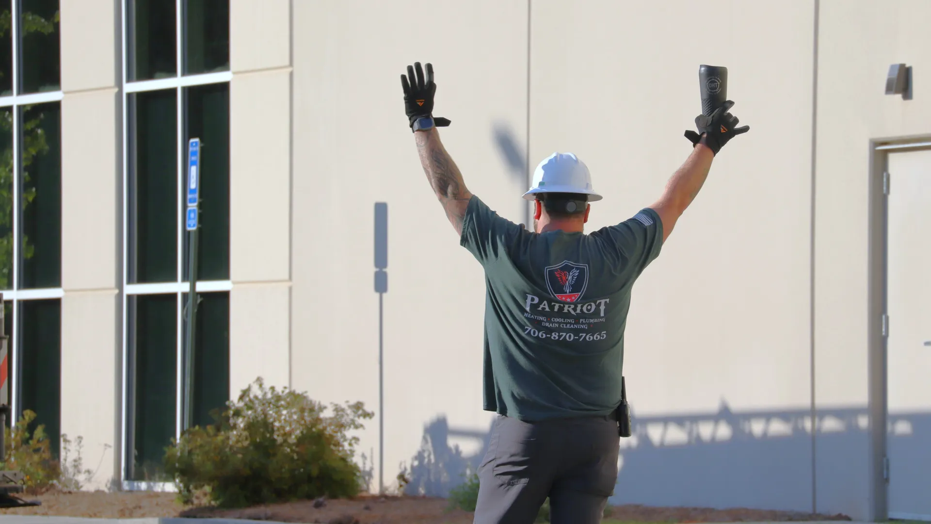 Construction worker in a hard hat raising arms in front of a building exterior during daytime