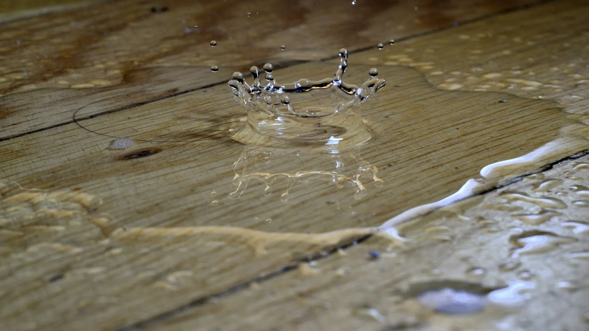 Water droplet splash creating a crown shape on a wet wooden surface with reflections and ripples.