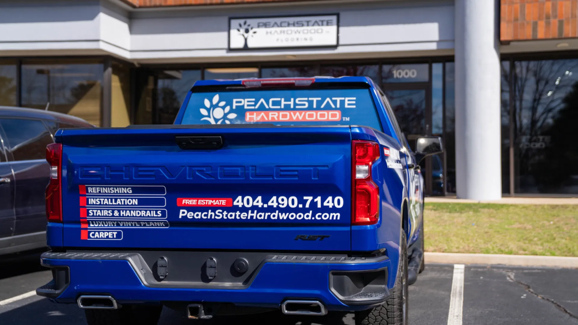 Blue Chevrolet truck with Peach State Hardwood advertisement parked outside company office with signage.