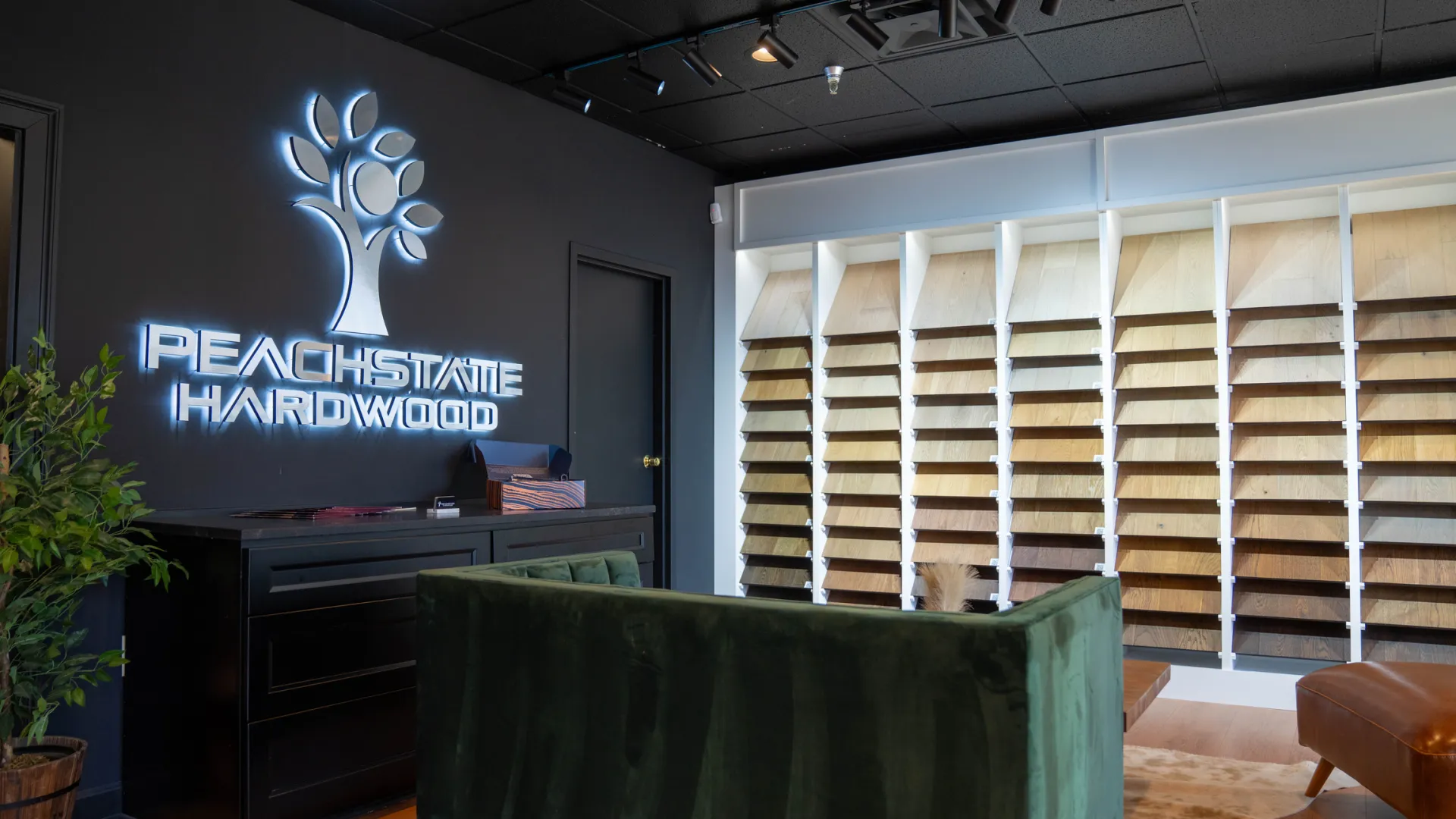 Modern hardwood showroom with illuminated Peach State Hardwood logo and wood samples displayed on the wall.