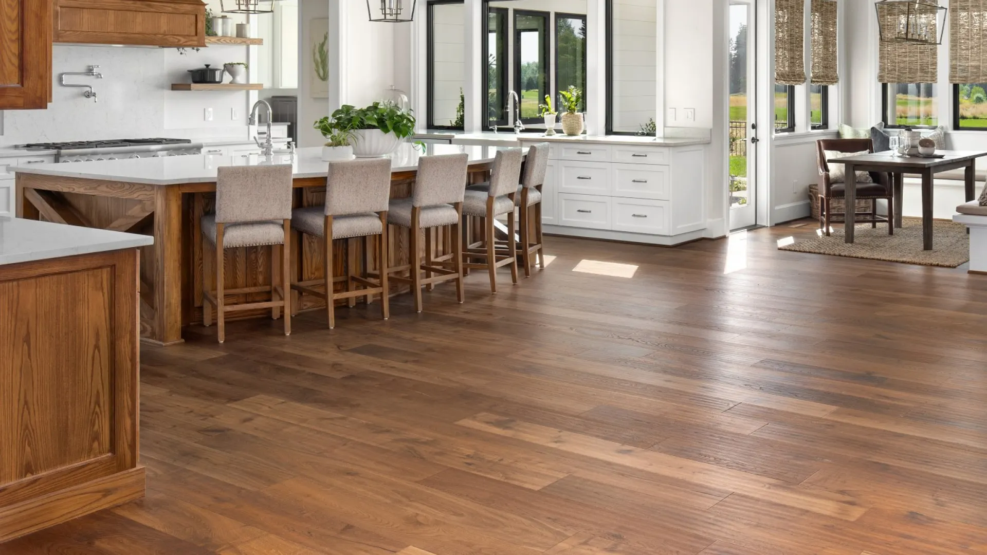 Spacious modern kitchen with wooden floors, white cabinetry, a large island with bar stools, and a dining area with natural light.