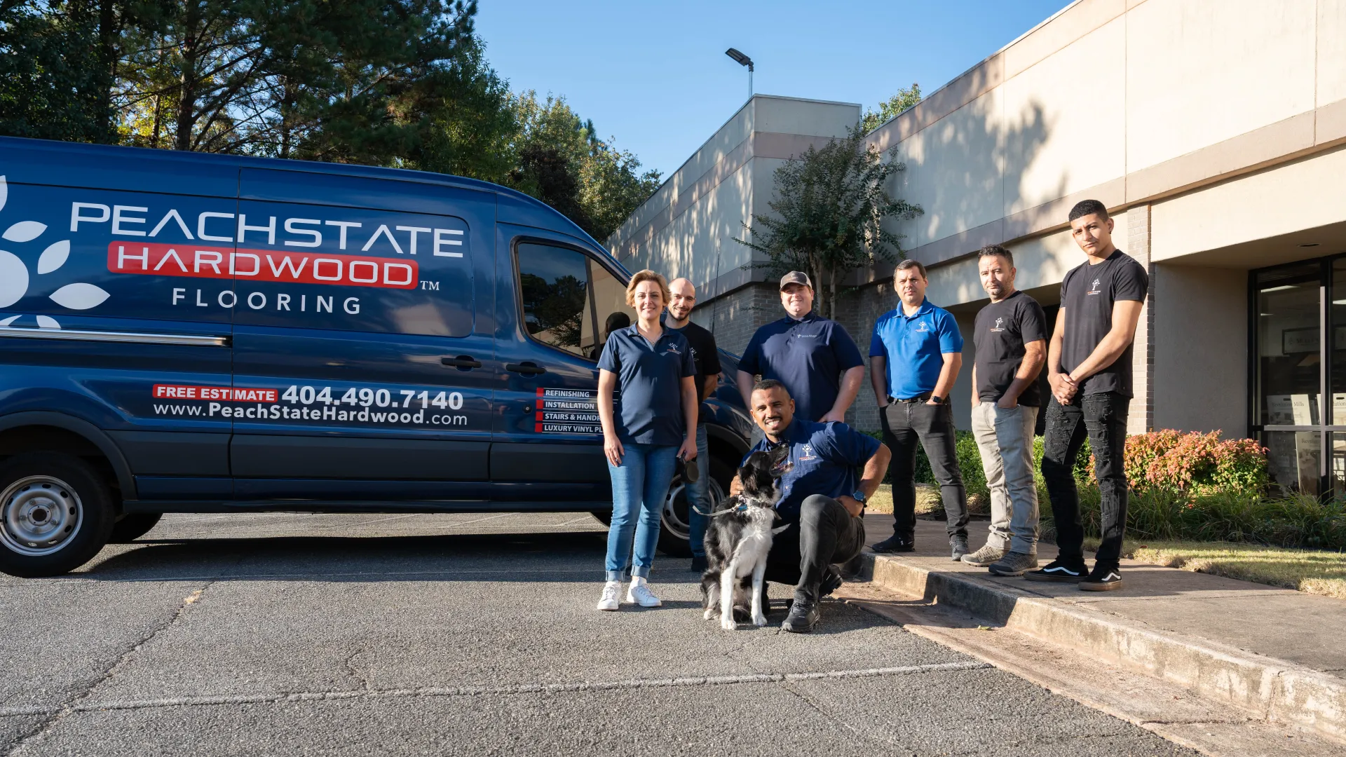 PeachState Hardwood Flooring team posing with a dog beside their branded service van outside a building on a sunny day.