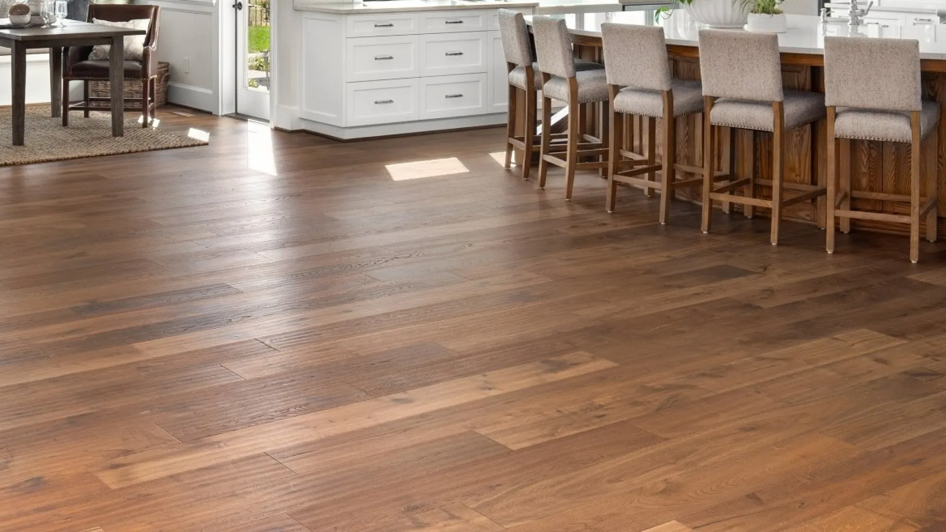 Spacious kitchen with natural wood flooring, white cabinetry, and wooden bar stools at a large island.
