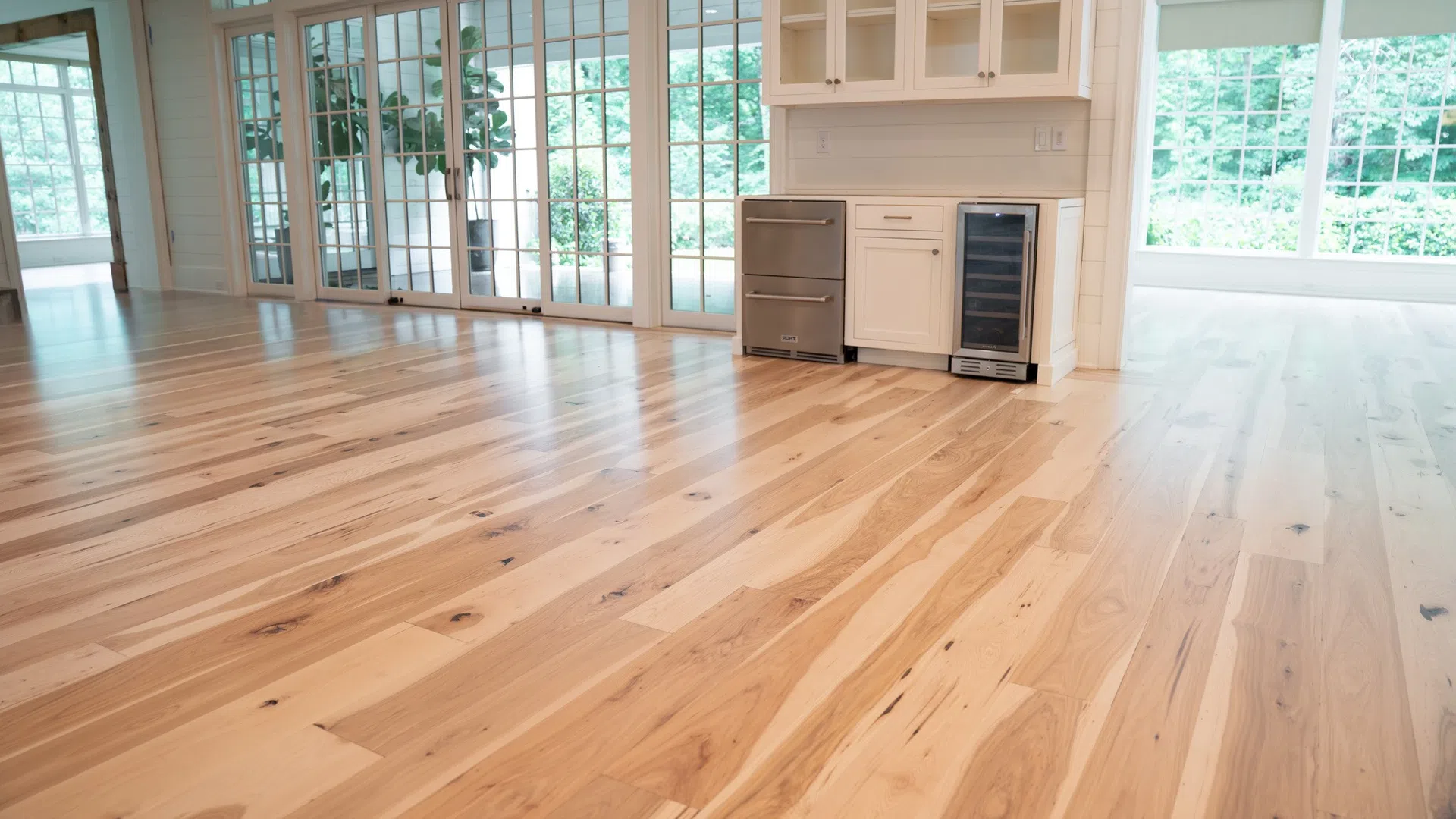 Spacious room with polished natural wood floors, white cabinetry, large windows, and glass sliding doors.