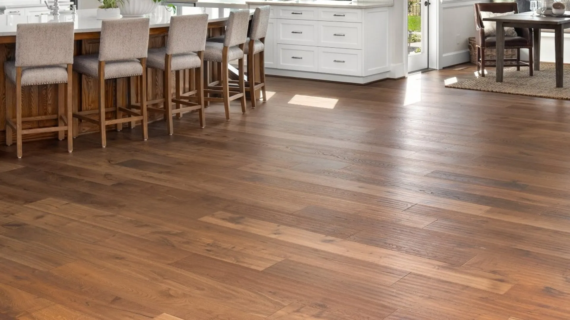 Bright open kitchen and dining area with wooden floors, white cabinetry, and modern furnishings in a spacious home.