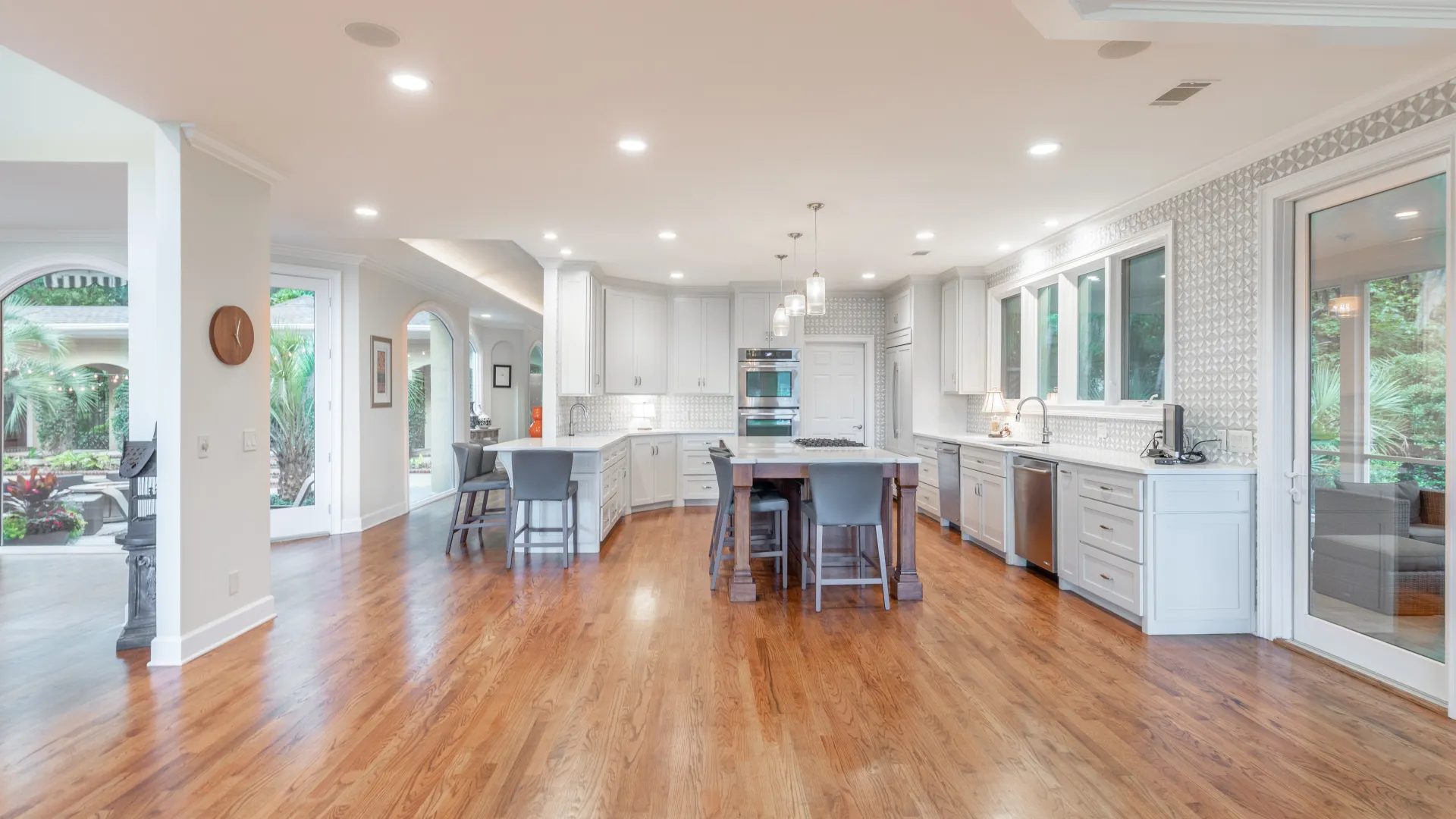 Spacious modern kitchen with hardwood floors, white cabinets, central island, and large windows overlooking garden.