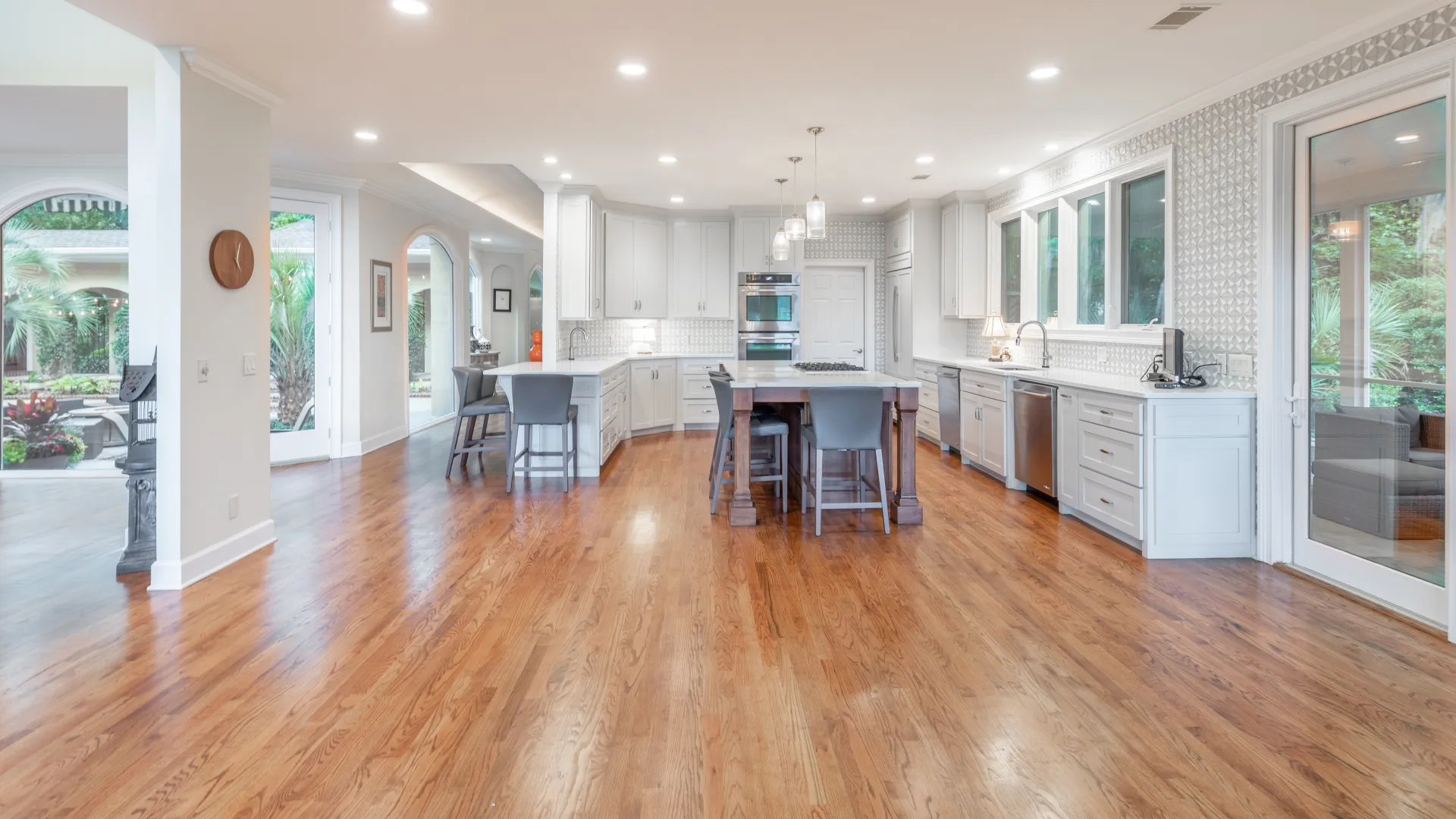 Spacious modern kitchen with hardwood floors, white cabinets, central island, and large windows overlooking garden.