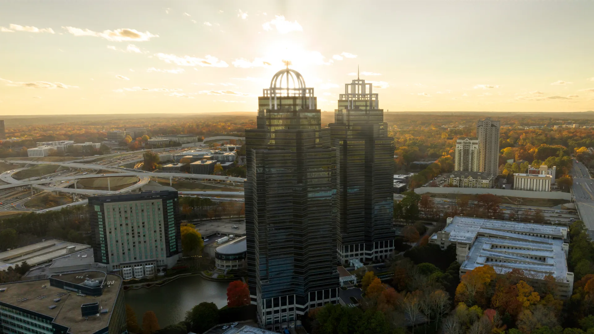 Aerial view of modern high-rise buildings surrounded by trees and roads during sunset in a cityscape.
