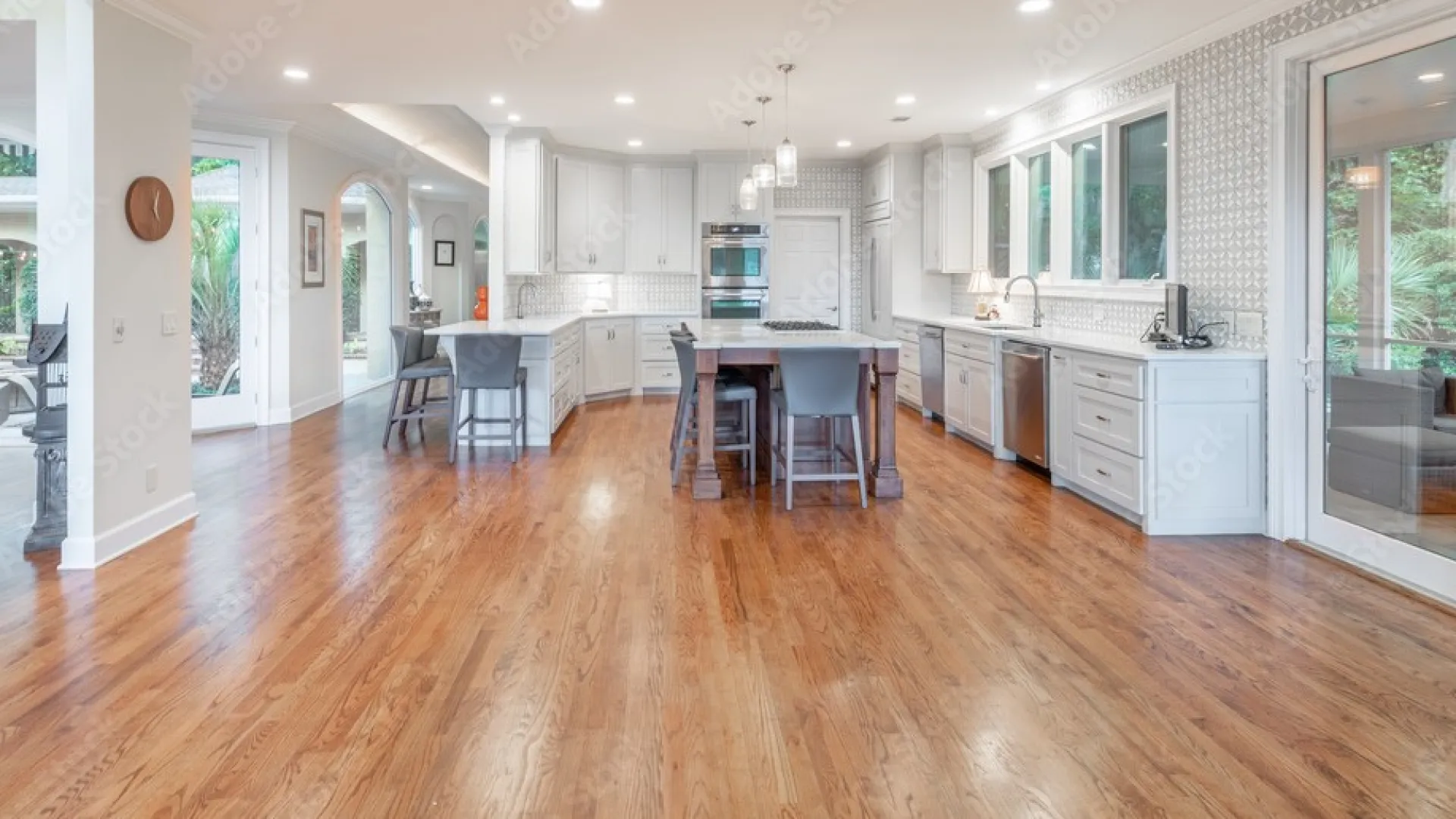 Spacious modern kitchen with white cabinets, kitchen island, hardwood floors, and large windows overlooking greenery.