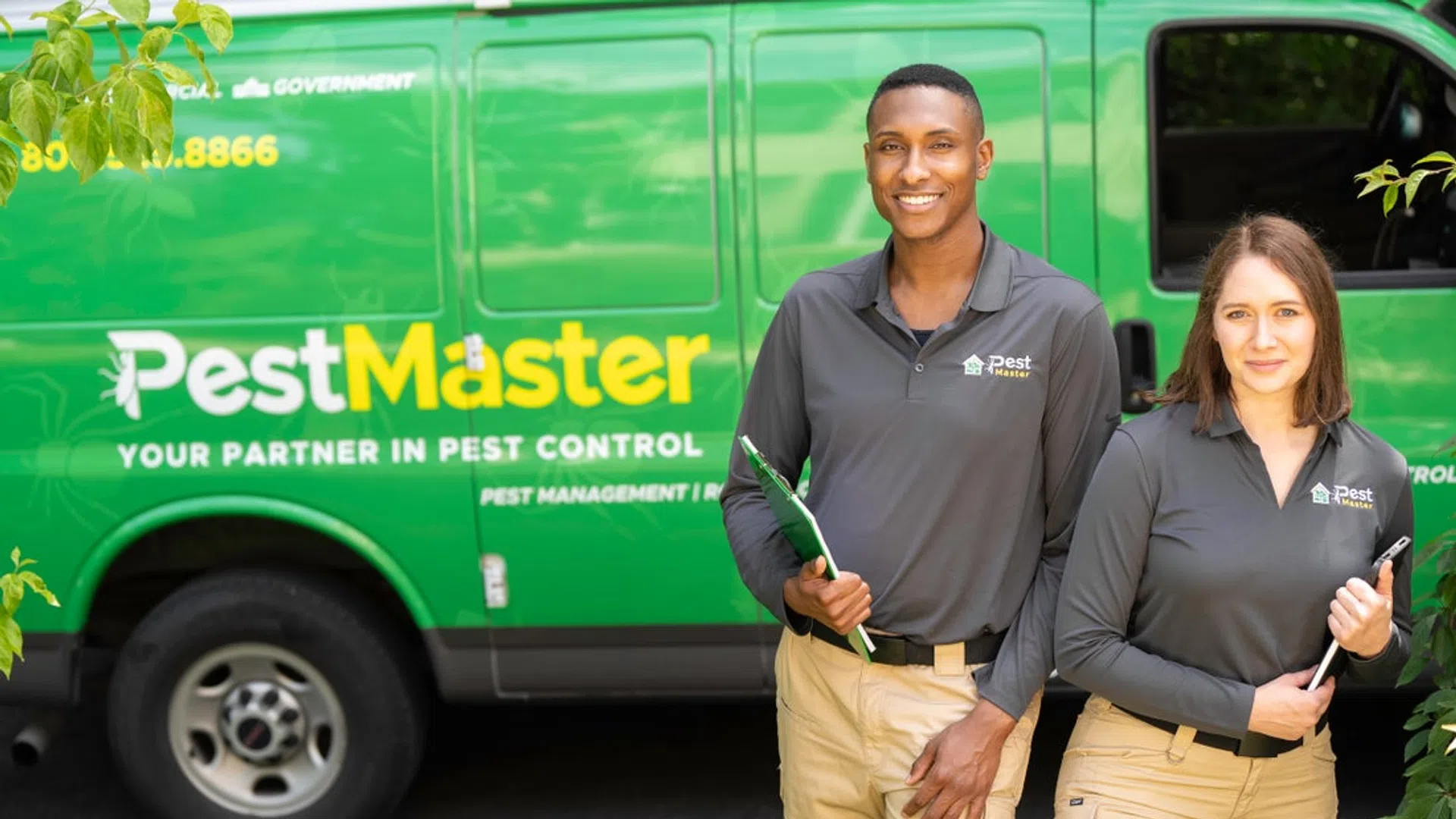 Two PestMaster pest control technicians in uniform standing in front of a green company van outdoors.