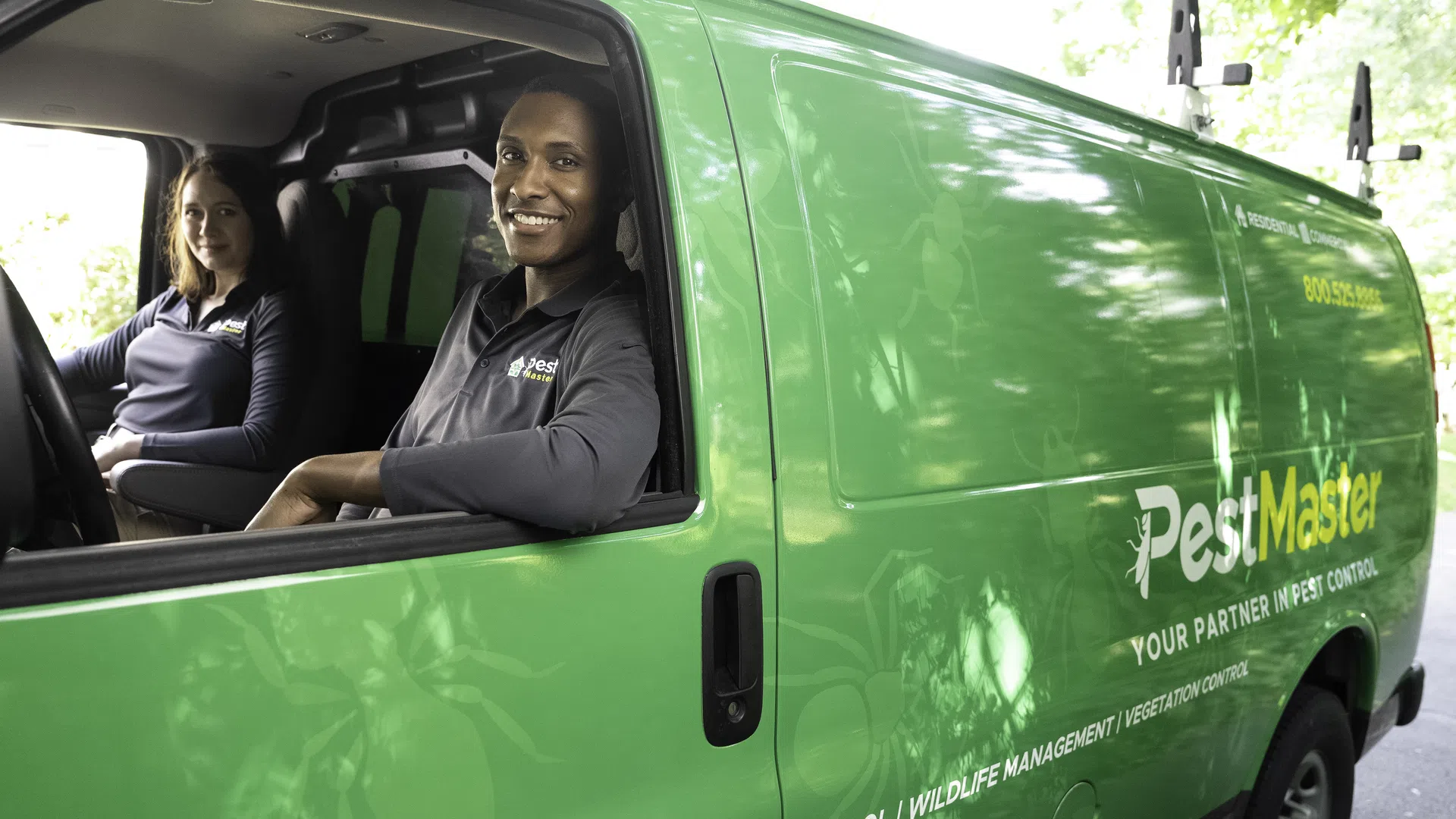 Two pest control professionals smiling from a bright green PestMaster van with company branding and contact info.