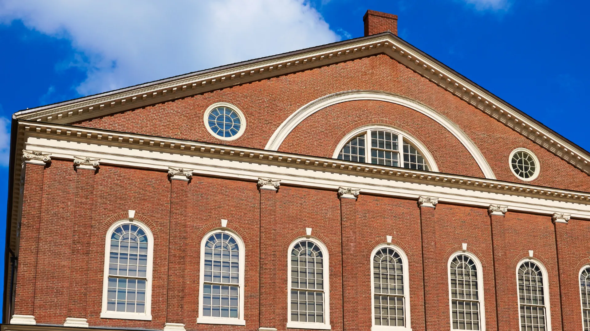 Historic red brick building with white trim and arched windows under a blue sky with clouds