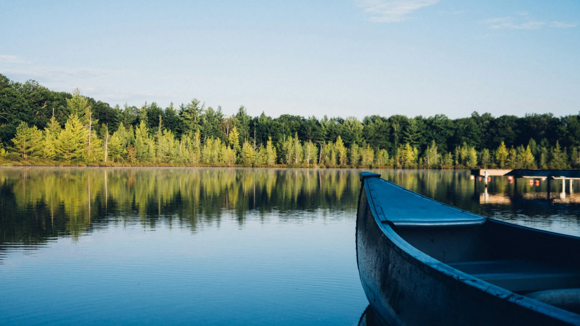 Calm lake with a canoe in the foreground and green trees reflecting on the water under a clear sky