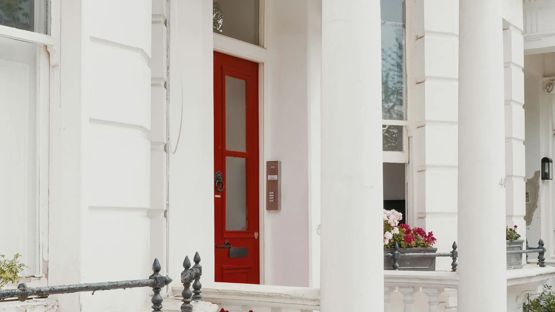 White classical townhouse with large columns and a striking red front door with glass panels.