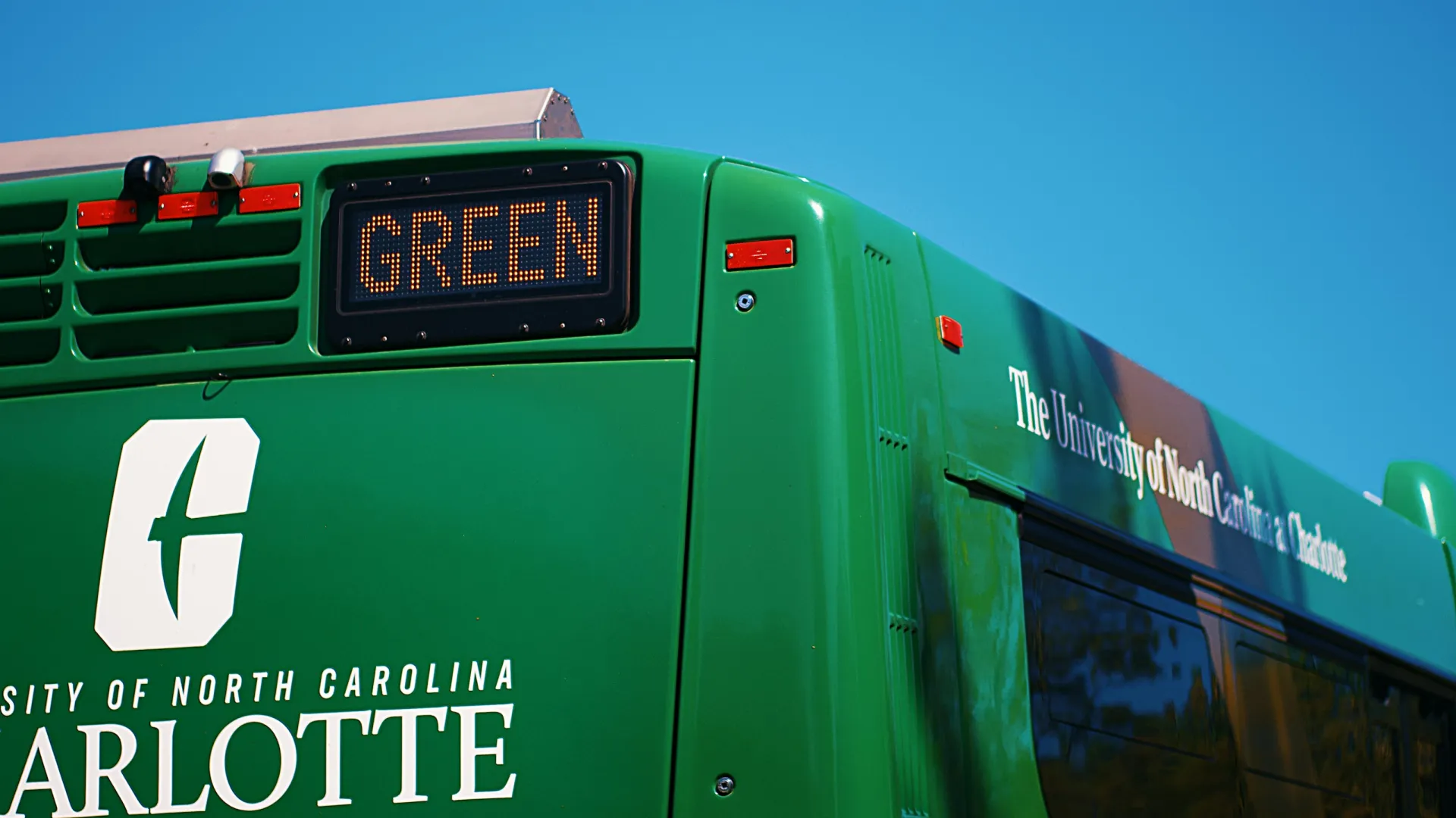 Green University of North Carolina Charlotte campus bus against clear blue sky