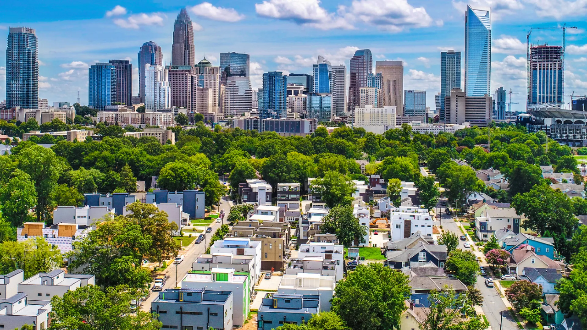 Panoramic view of Charlotte skyline with residential area and lush green trees under blue sky with clouds