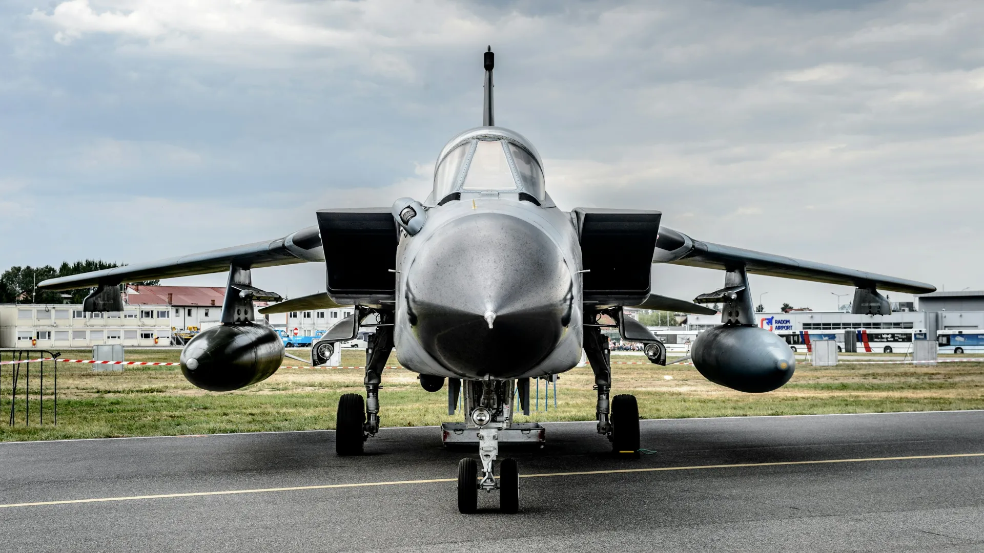 Front view of a military jet fighter parked on a runway under a cloudy sky