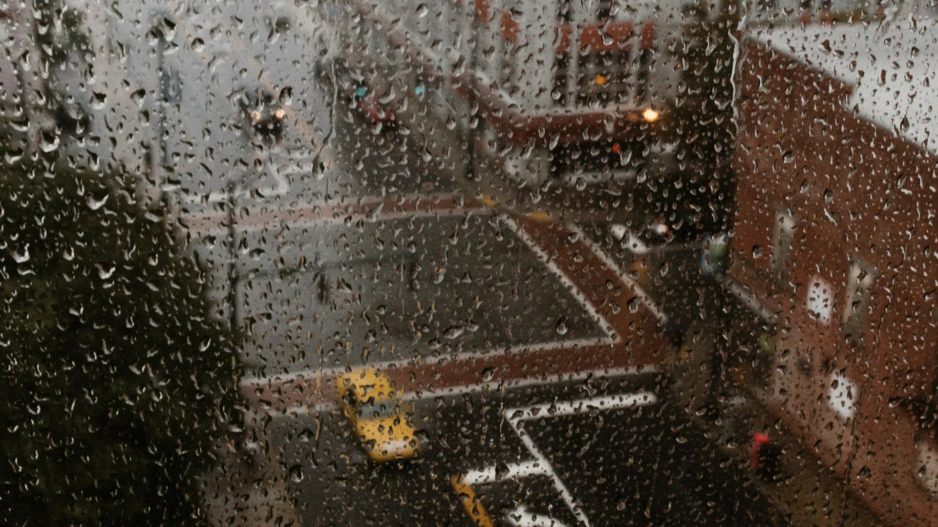 Rain drops on window overlooking a city street with cars and tall buildings on a gloomy day