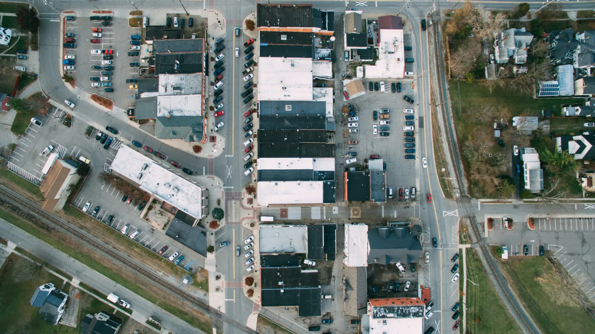 Aerial view of a small town with roads, buildings, parking lots, and train tracks intersecting the area.