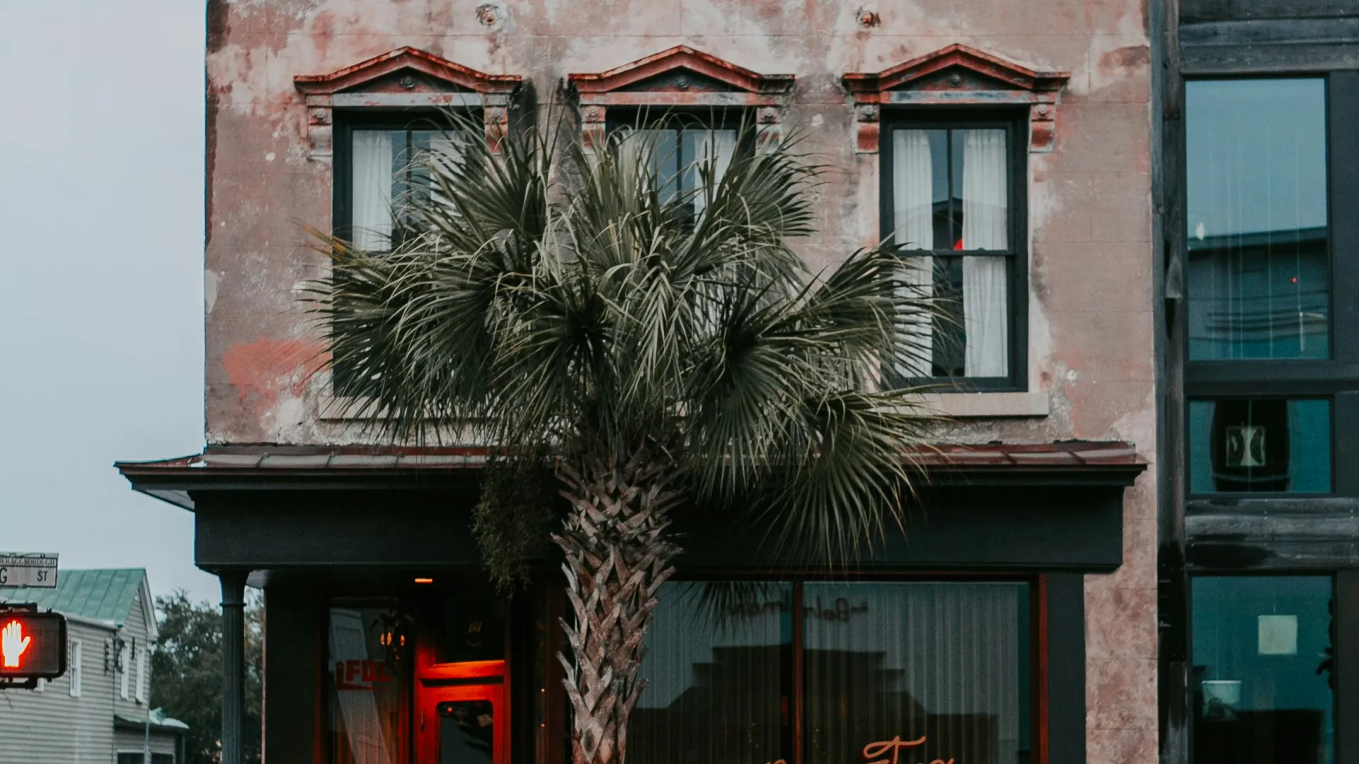 Three-story aged building with palm tree in front and neon sign reading Town Ninety Two.