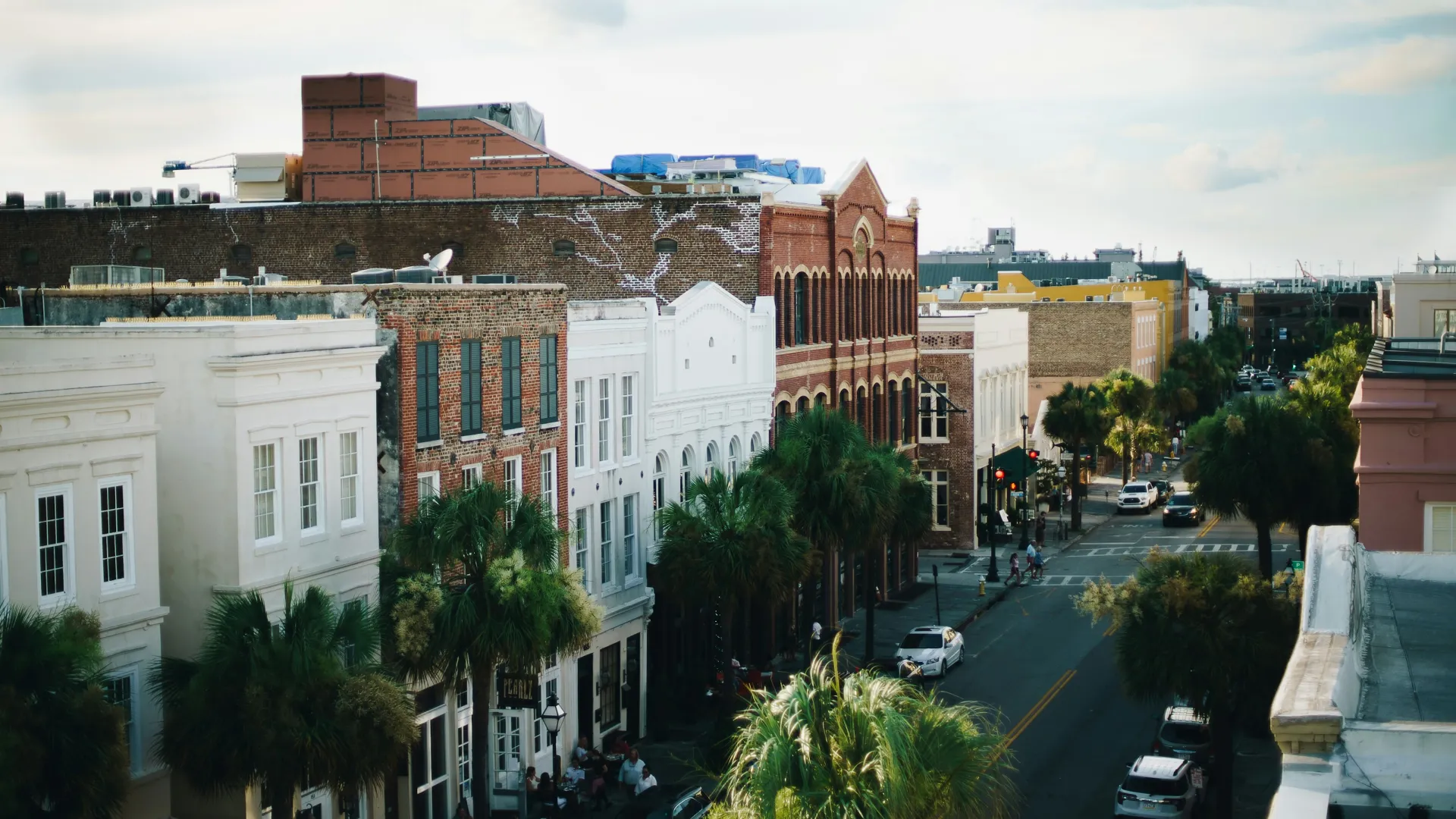 Historic street lined with brick and white buildings, palm trees, and parked cars on a sunny day.