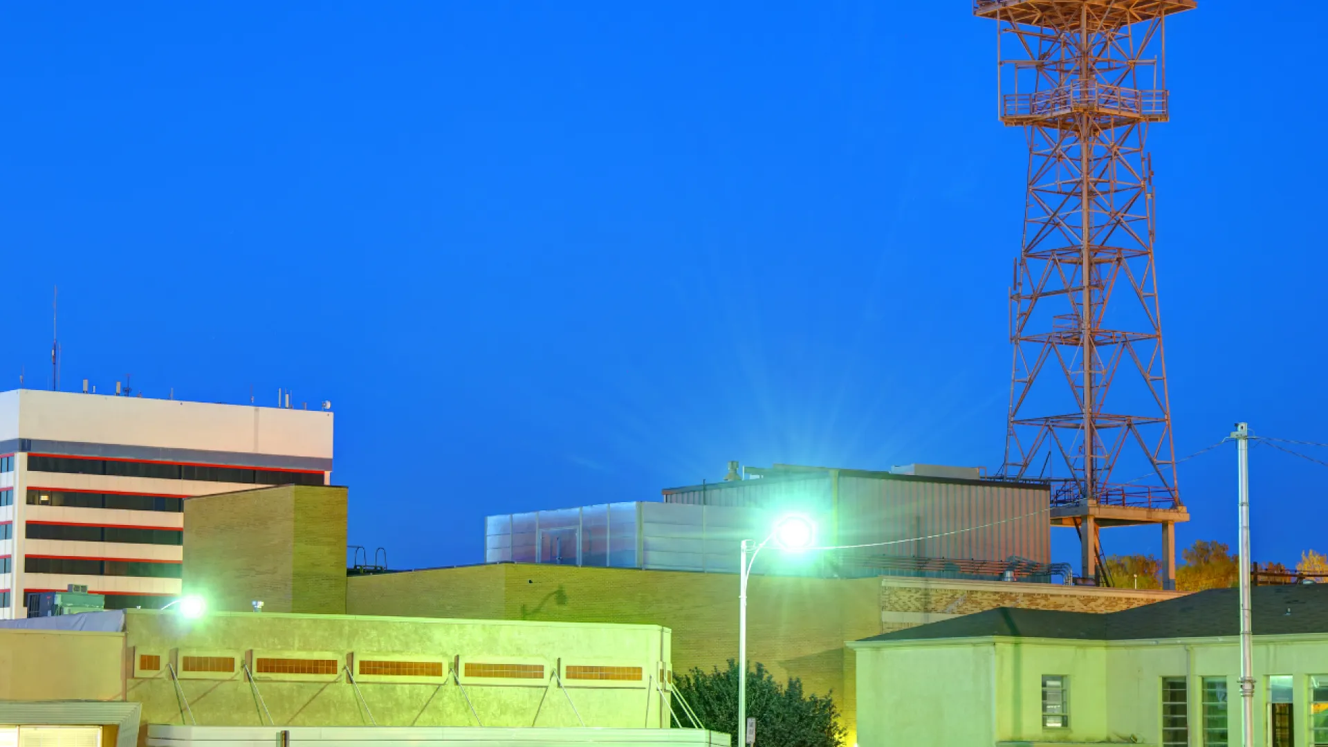 Cityscape at dusk with modern buildings under a clear blue sky and communication tower in background