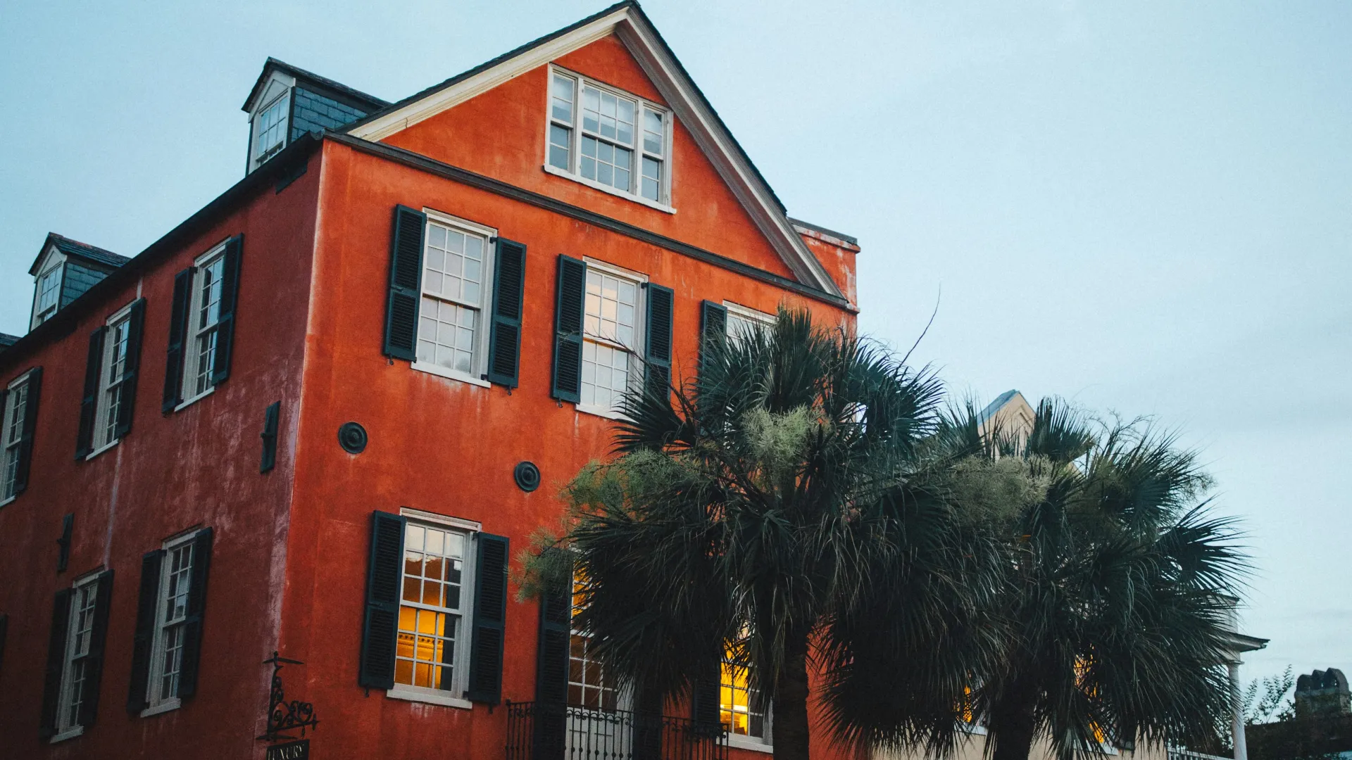 Historic red and beige buildings with lit windows and palm trees at dusk on a quiet street.