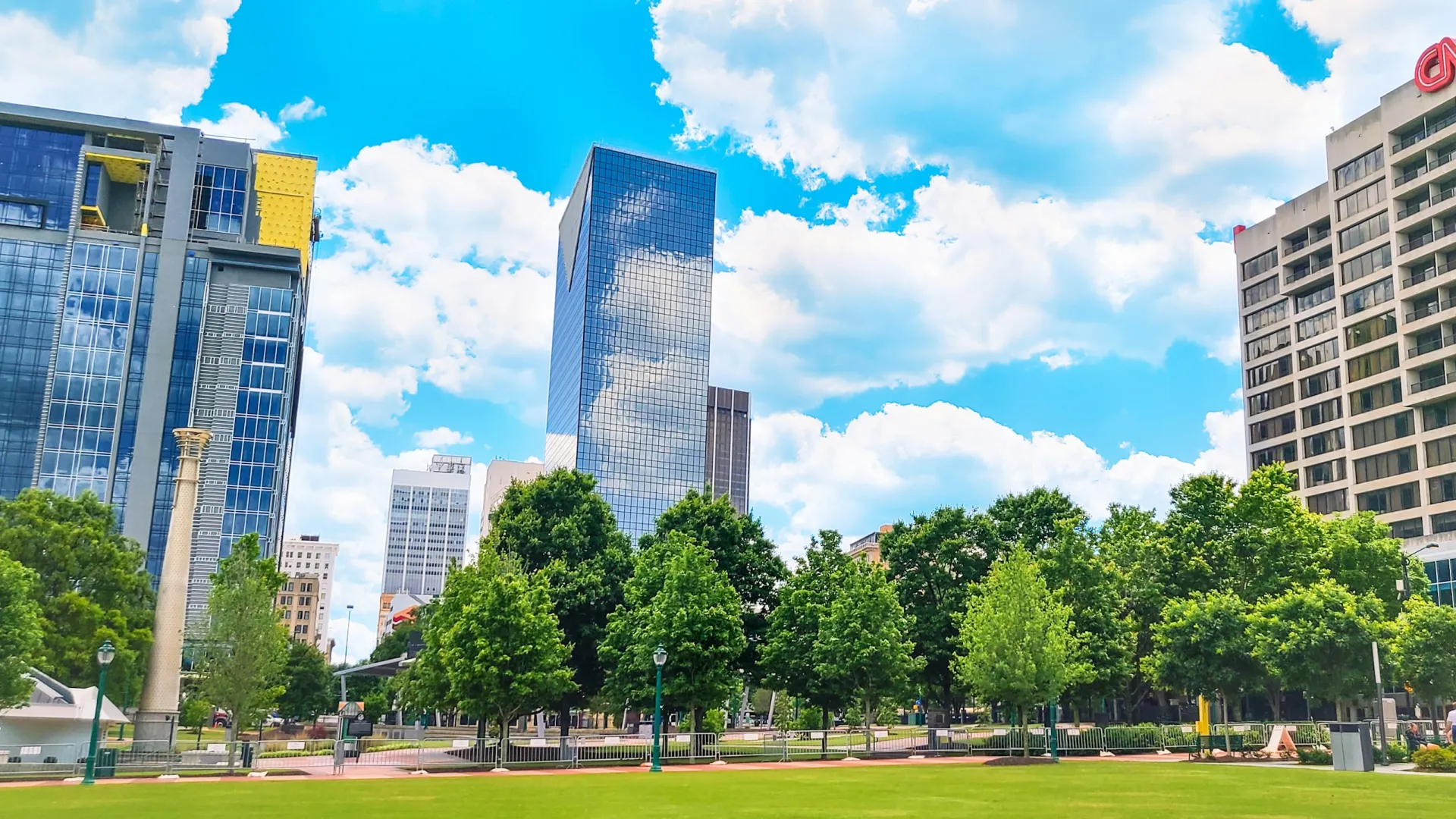 City park with lush green trees and skyscrapers including CNN building under a bright blue sky with clouds