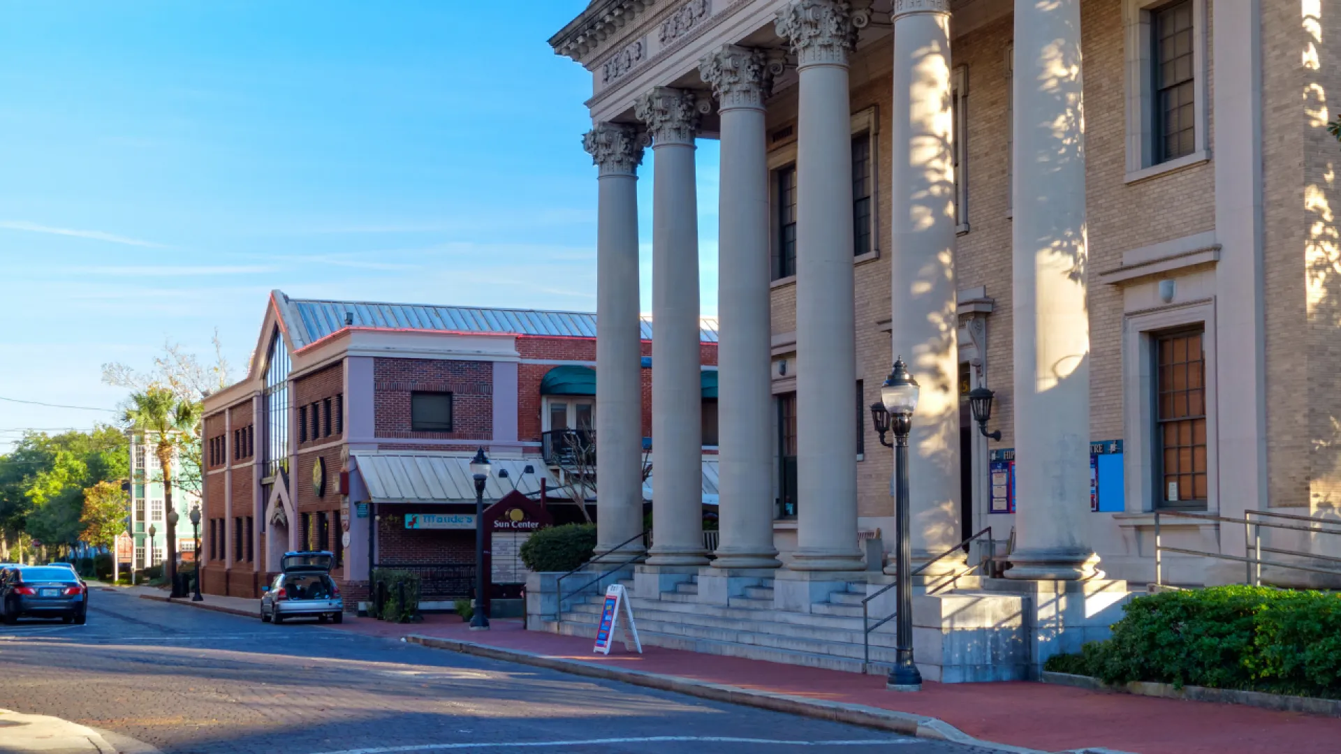 Historic downtown street with classic buildings, columns, parked cars, and clear blue sky on a sunny day