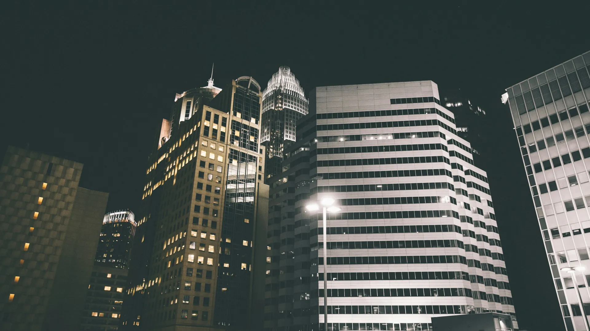 Night view of illuminated tall office buildings in a modern city skyline with street lights in foreground
