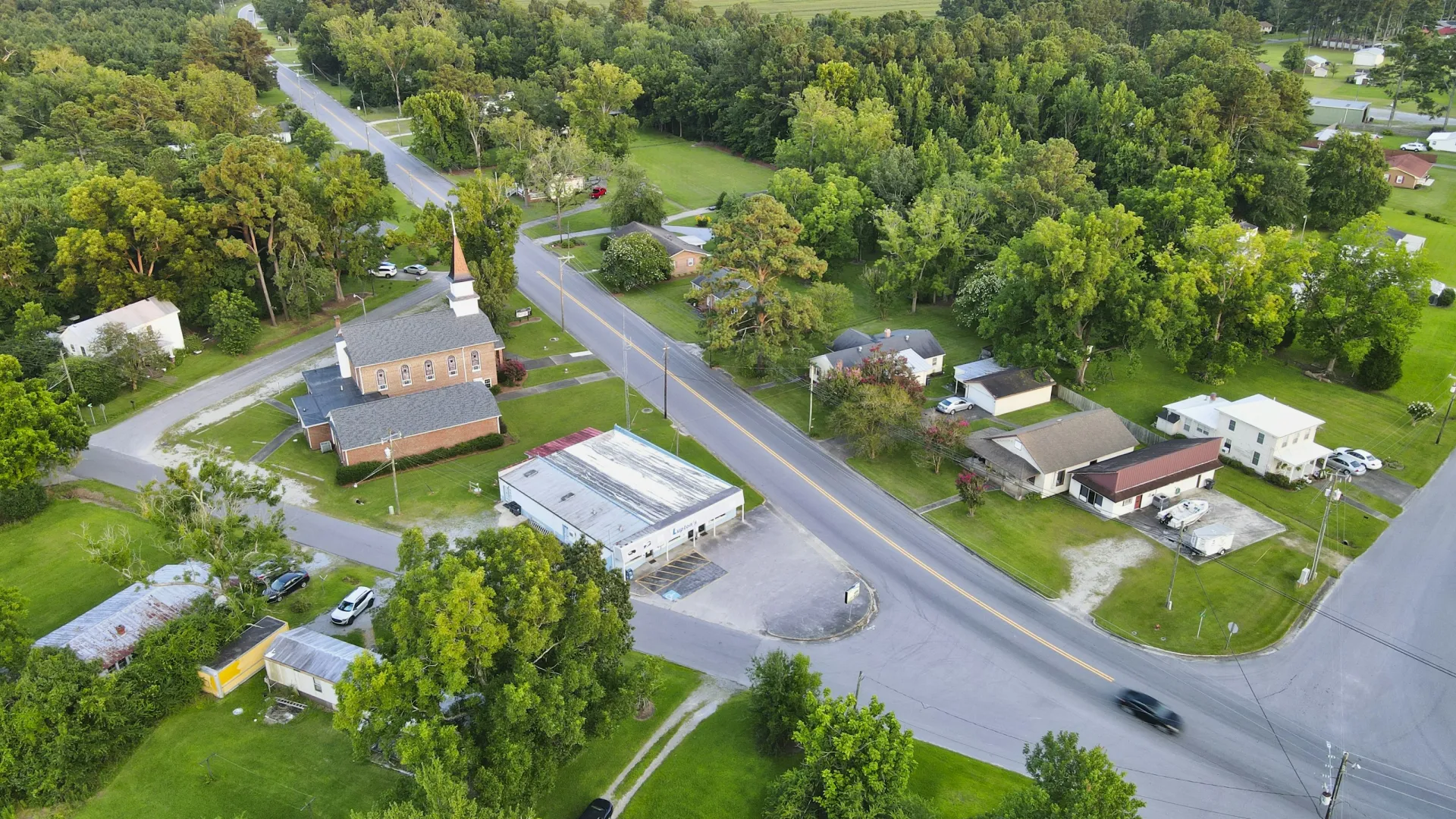 Aerial view of a small rural town with houses, a church, roads, and surrounding green trees and fields
